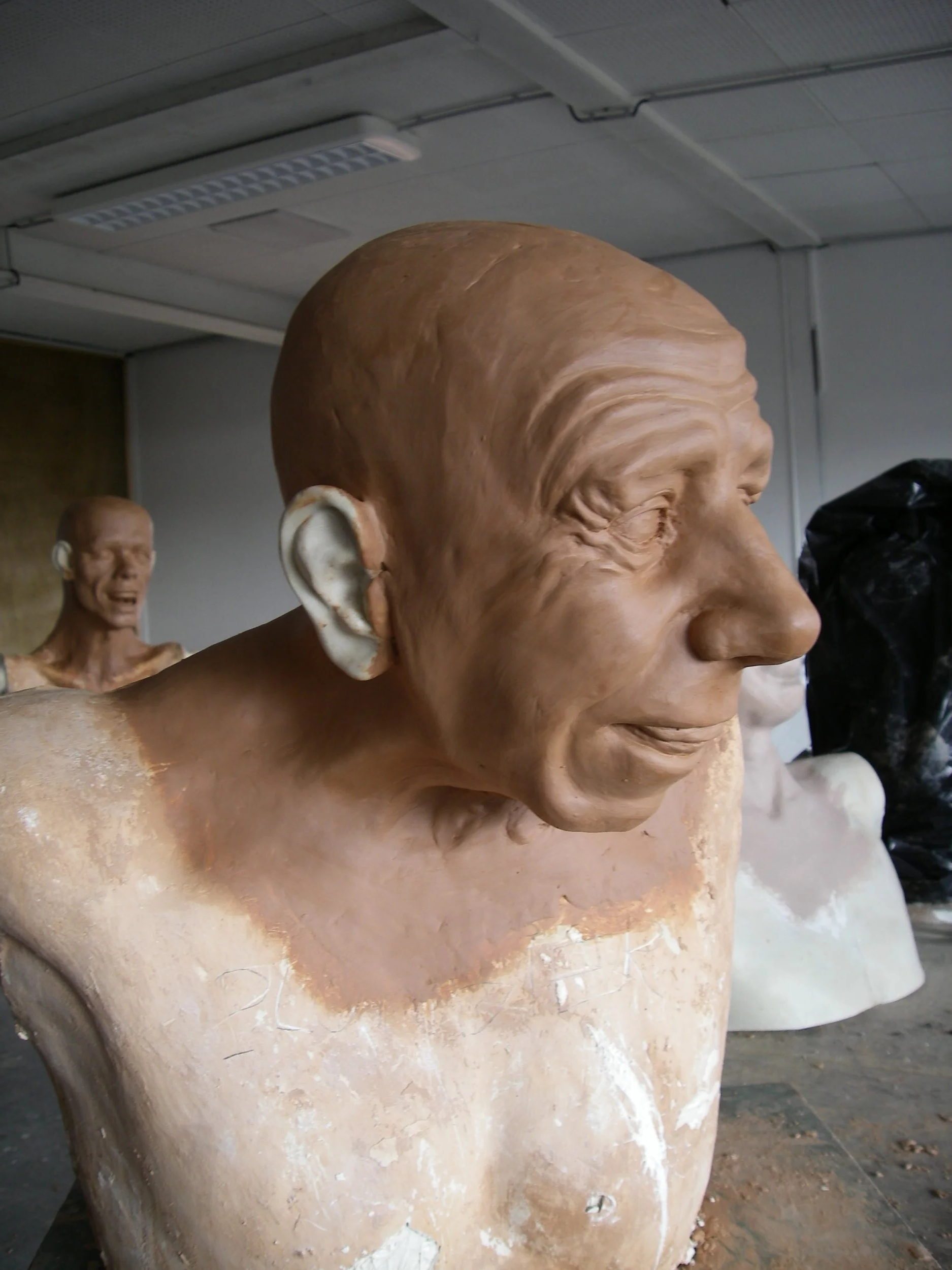 Buste en cours de fabrication représentant un homme âgé avec des détails réalistes, texture en argile ou plâtre, dans un atelier de sculpture.