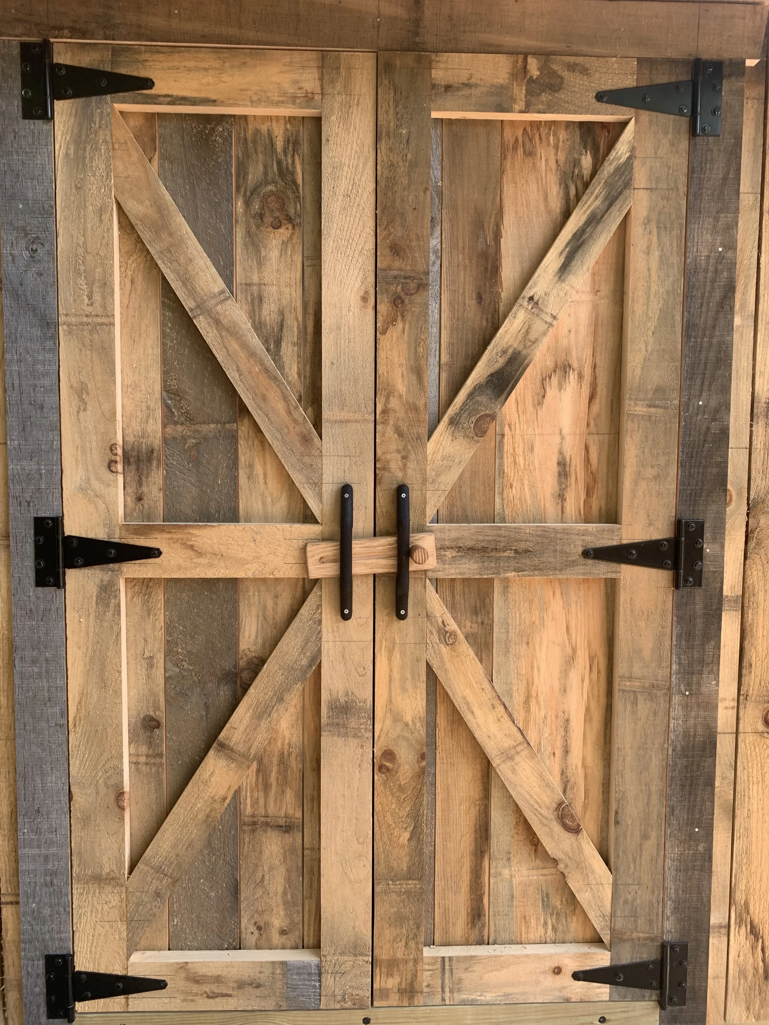 A wooden barn door with black metal hinges and handles, featuring a diagonal cross-brace for support.