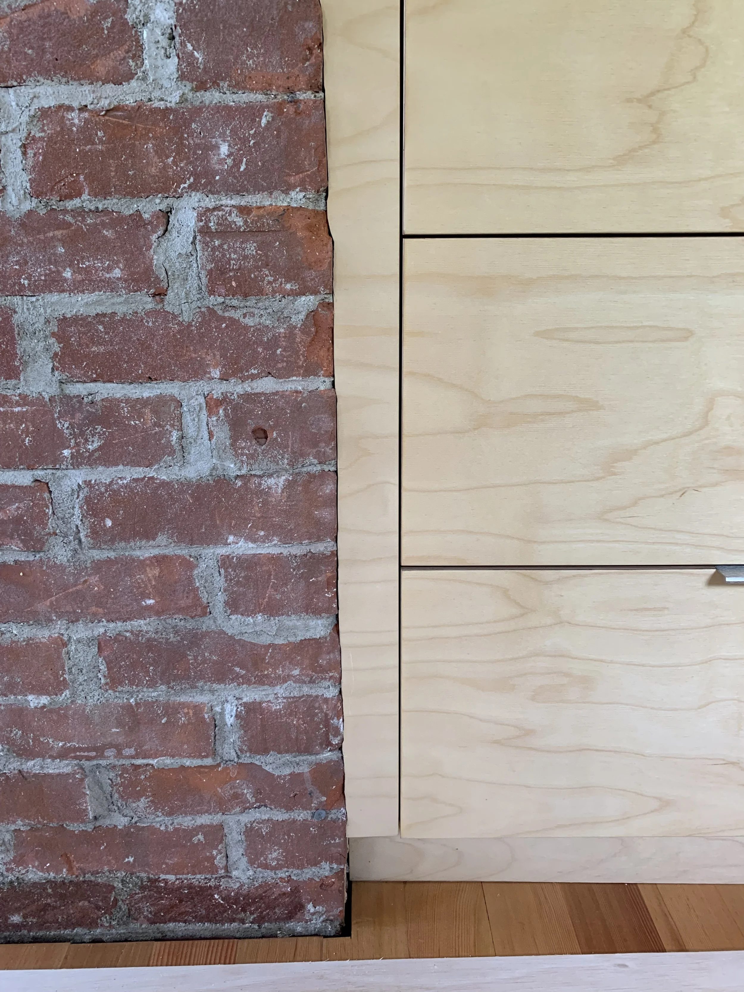 Close-up of a wall with exposed red bricks on the left and a wooden cabinet with light-colored wood panels on the right.