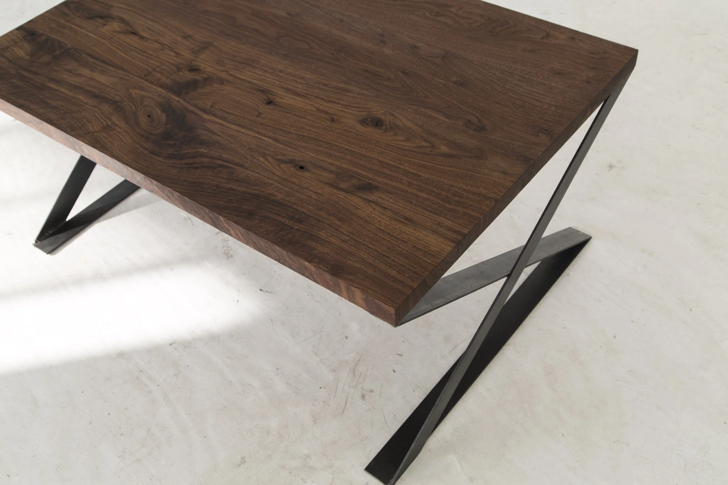 A modern desk with a dark wood surface and black zigzag metal legs on a white floor.