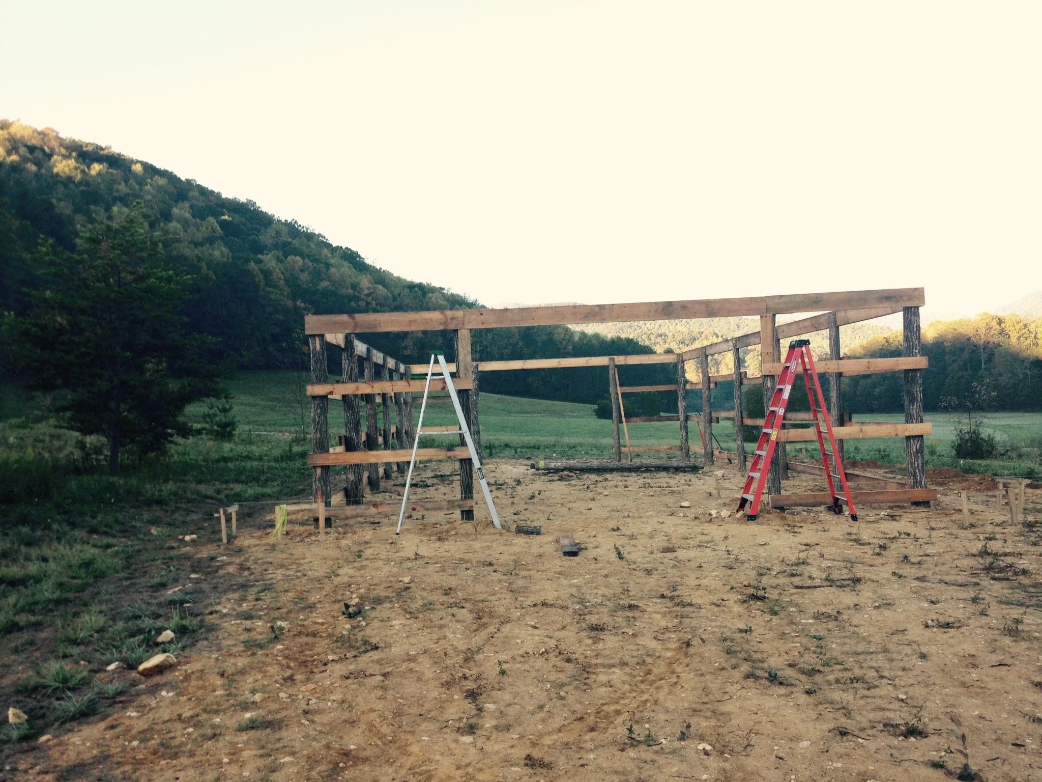 Construction site with wooden frame structure, two ladders, and mountainous landscape in the background.