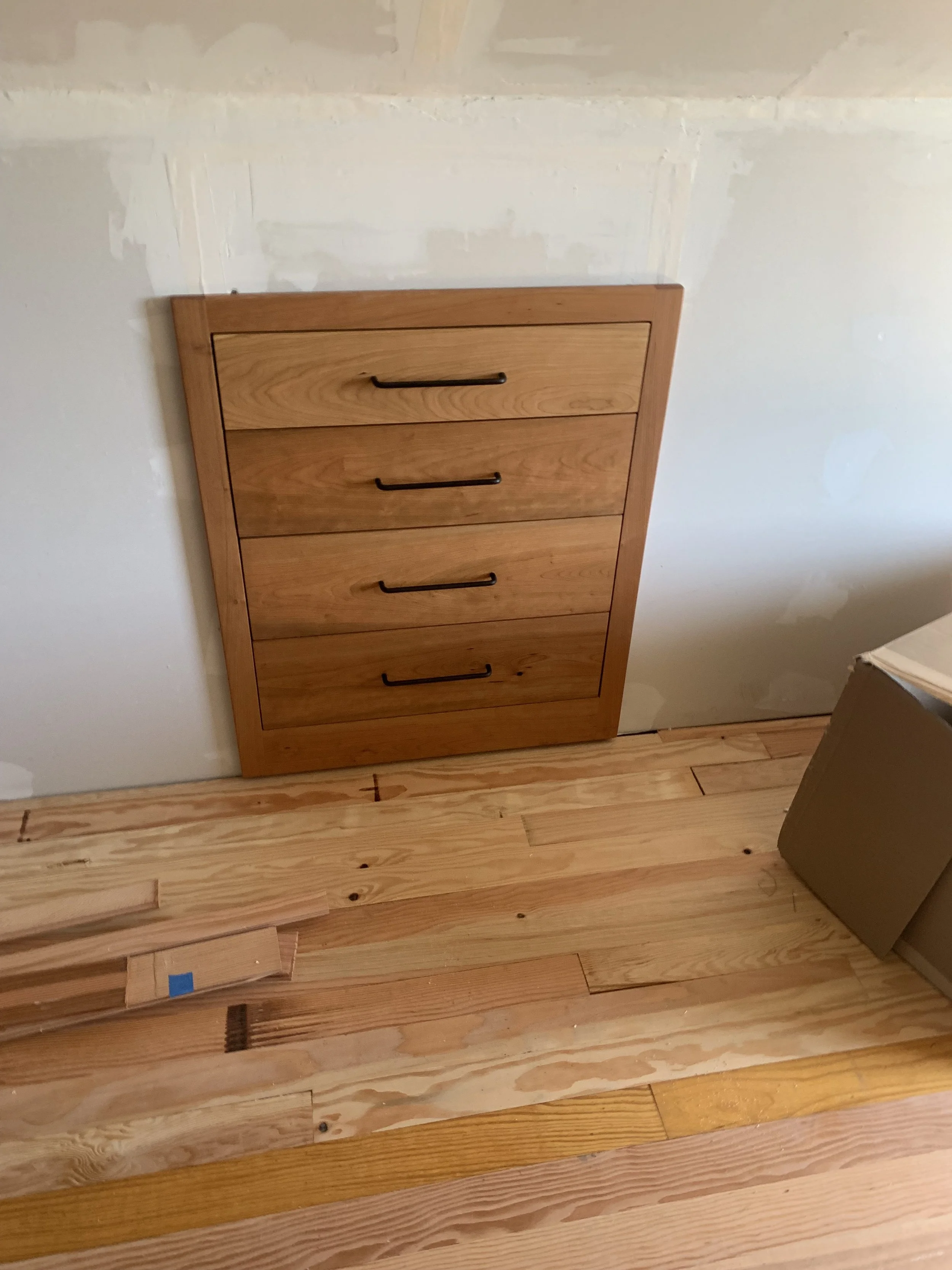 A wooden drawer installed on a white drywall wall with a light wood floor underneath.