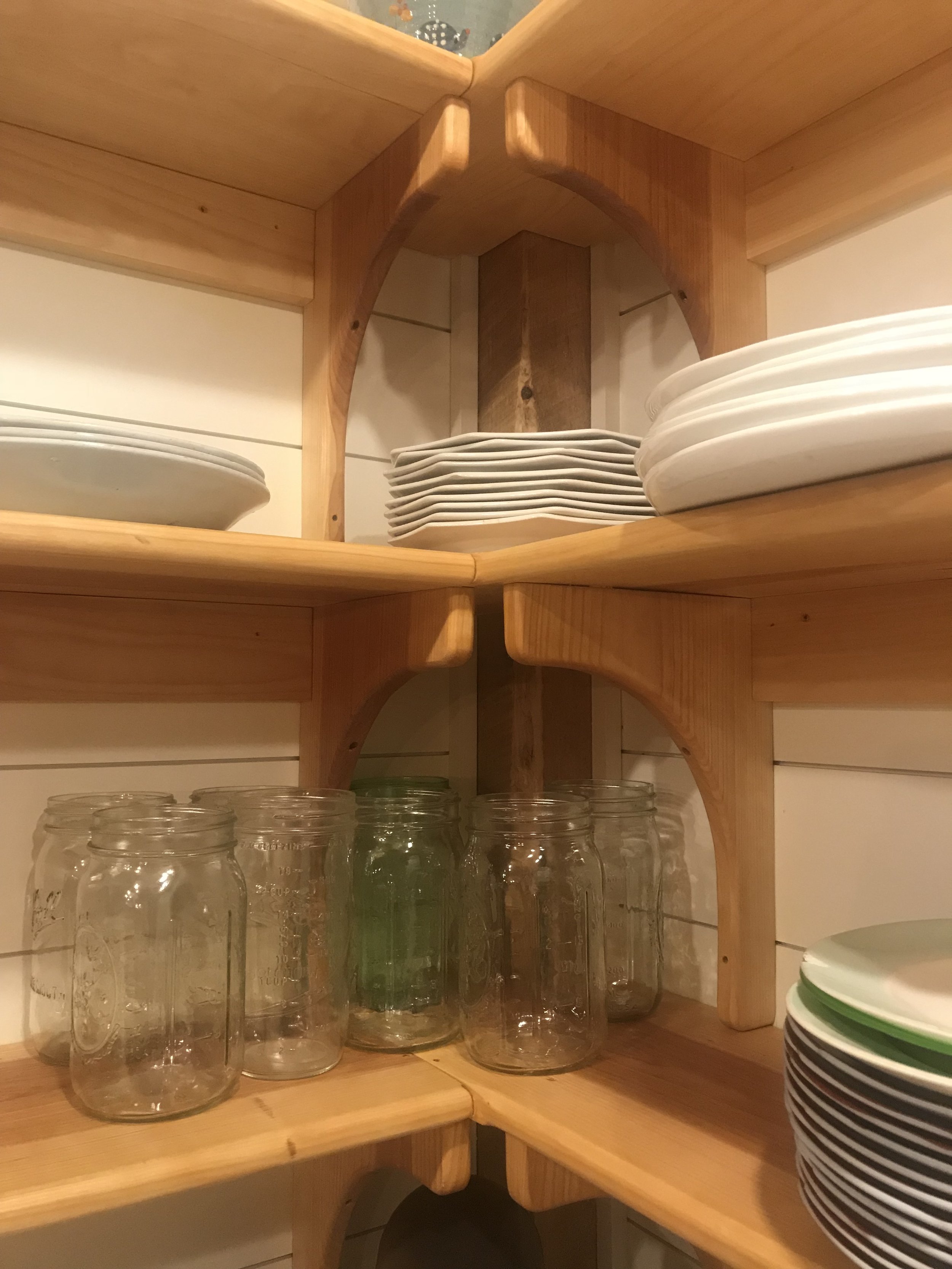 Wooden kitchen shelves holding stacks of white and black plates and clear glass jars.