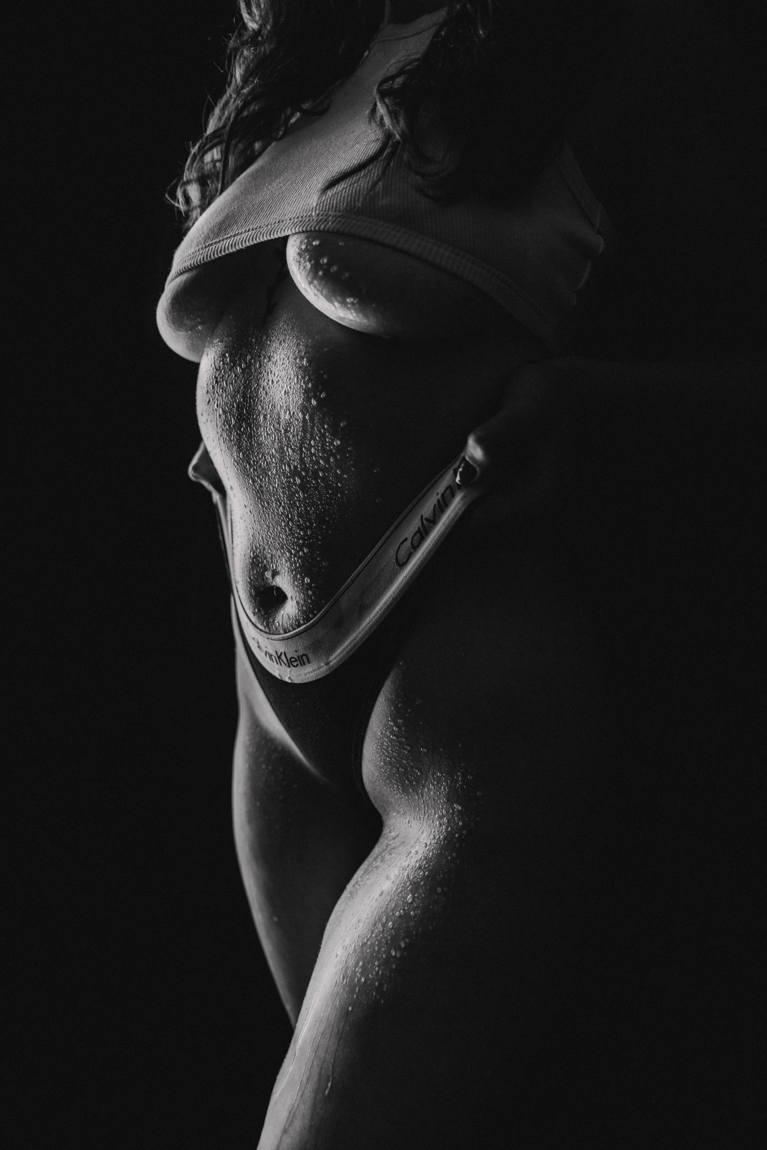 Close-up of a woman’s wet, toned body with a Calvin Klein waistband, with water droplets on her skin, in black and white.