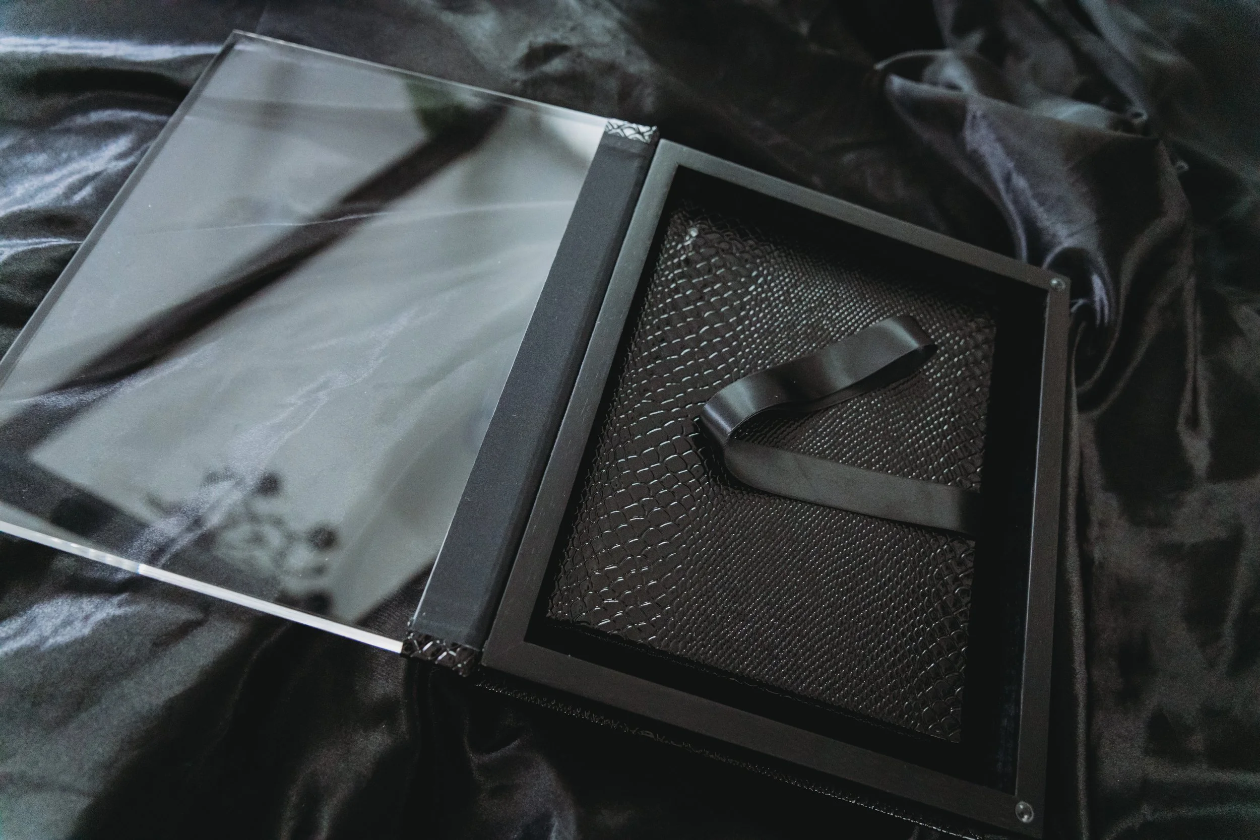 Black box with a clear lid and interior black mesh compartments, placed on black fabric.