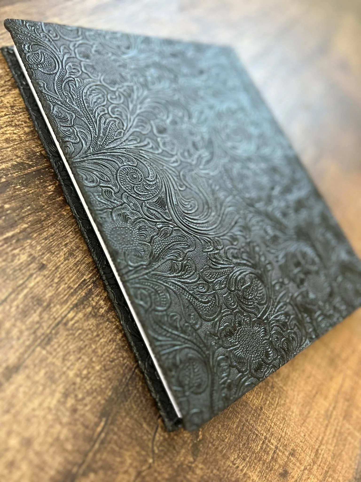 Close-up of a book with an embossed black cover featuring intricate floral and swirling patterns, placed on a wooden surface.