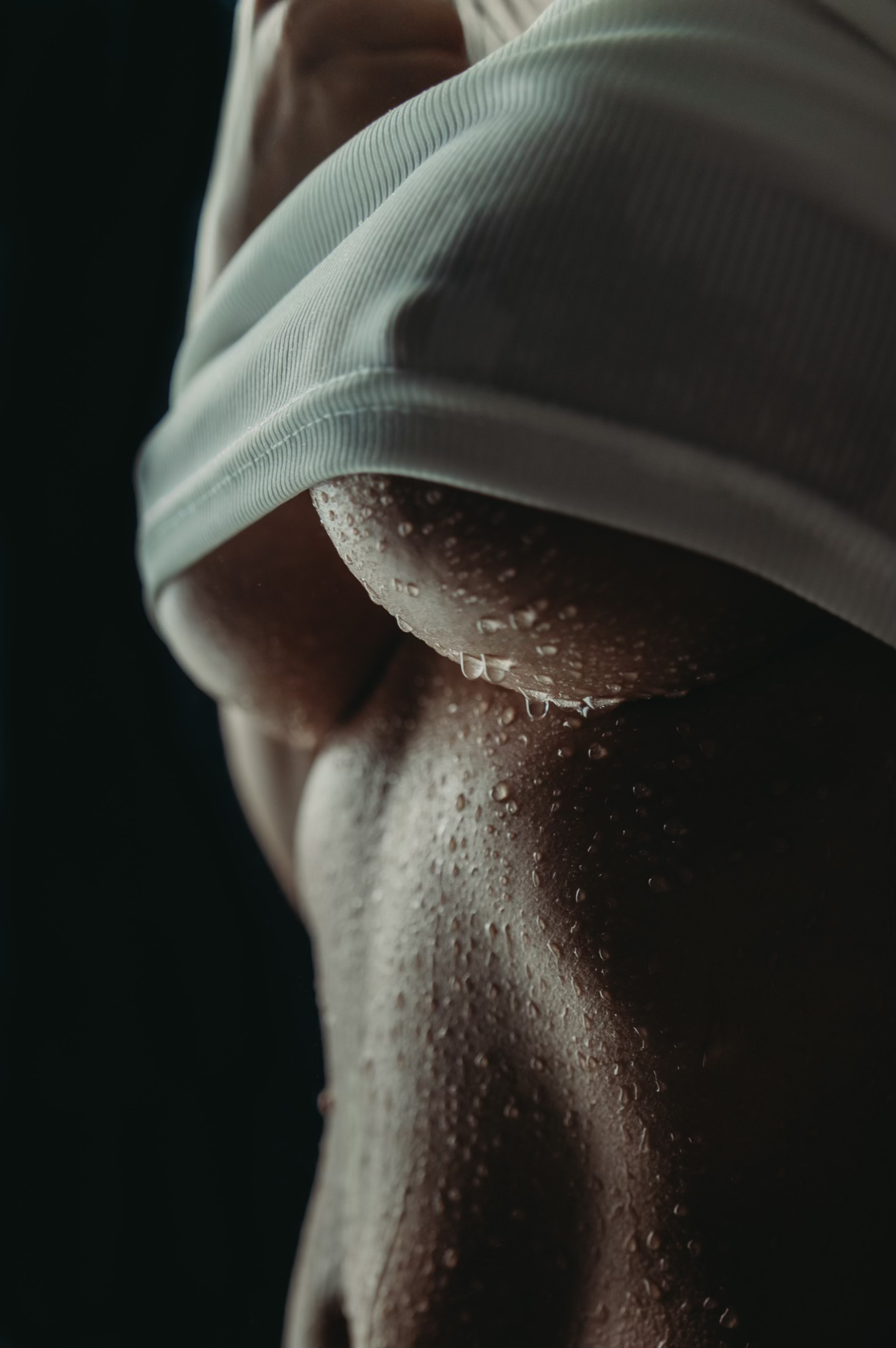 Close-up of a person's toned abdomen with water droplets, wearing a white sleeveless top.