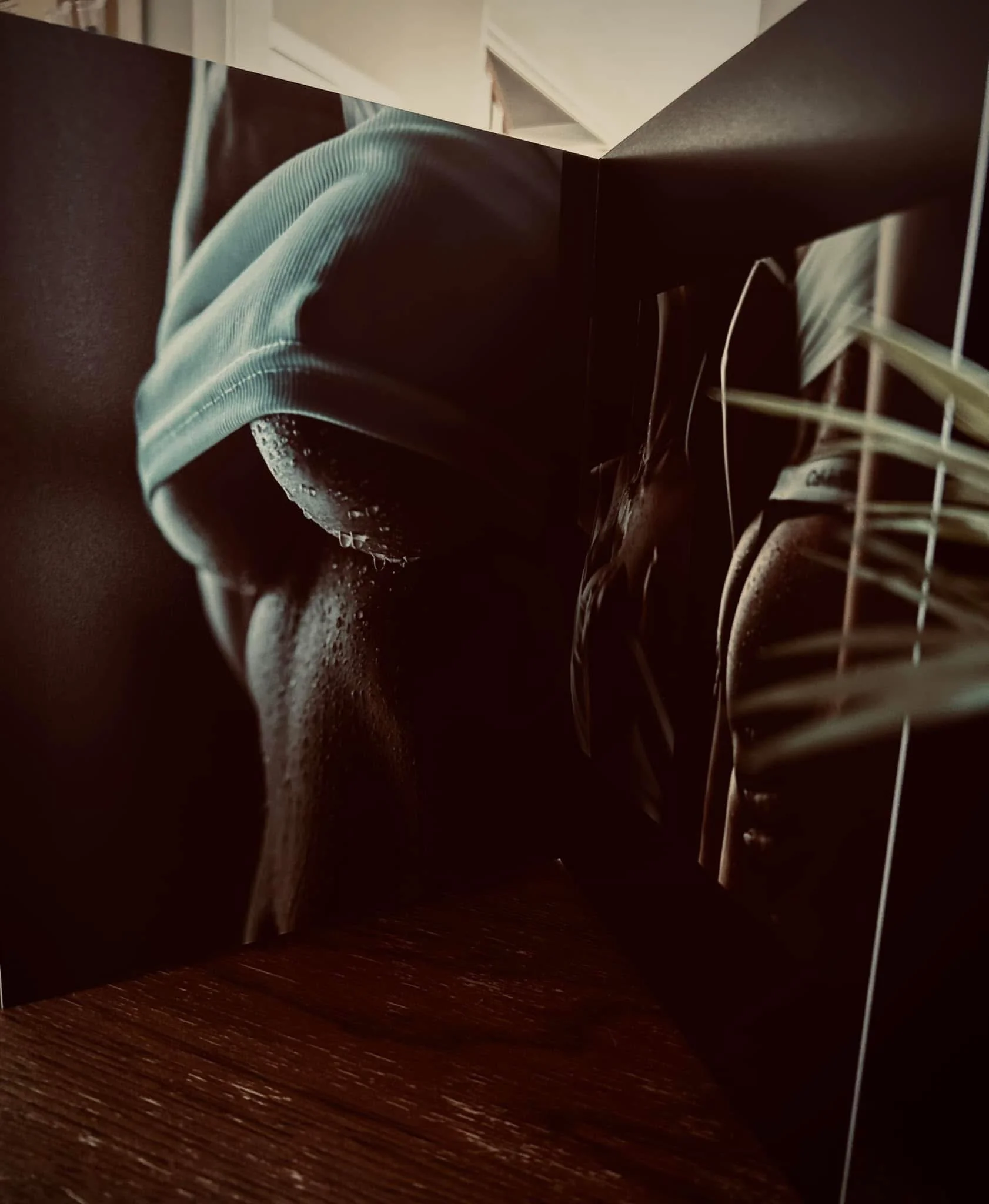 Close-up of a person in a light blue hoodie, wet from water, with a focus on the covered head, with raindrops or water droplets on the face and hoodie. The image is dark and moody, emphasizing textures and shadows.