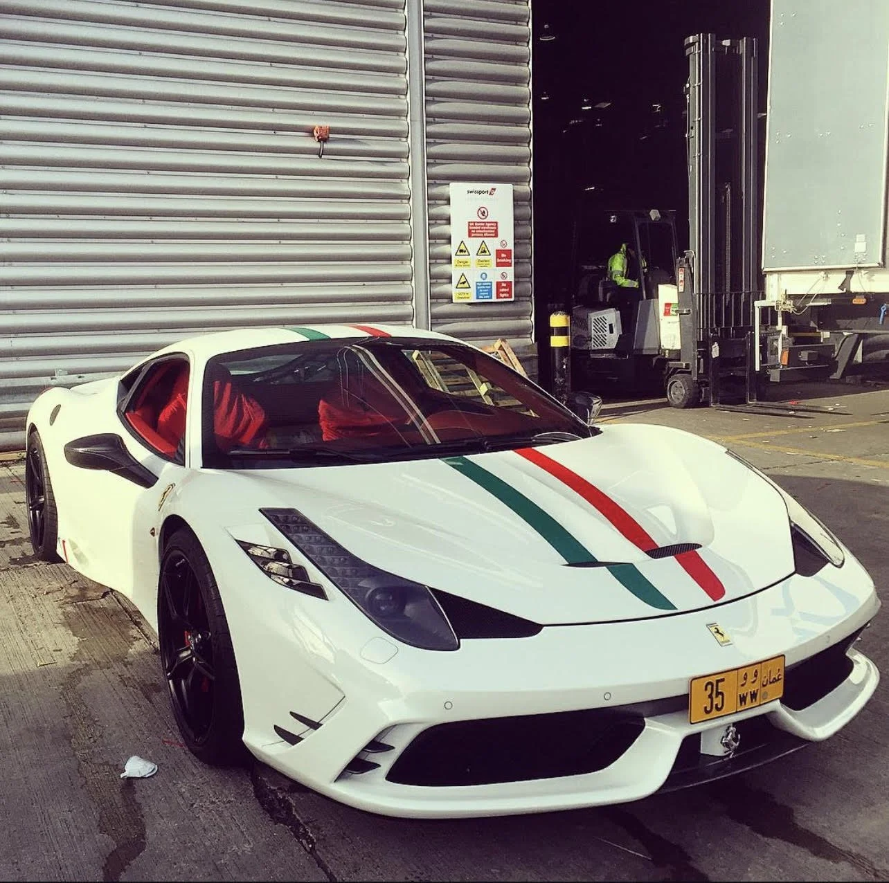 A white Ferrari sports car with Italian flag-themed stripes parked outside a building.