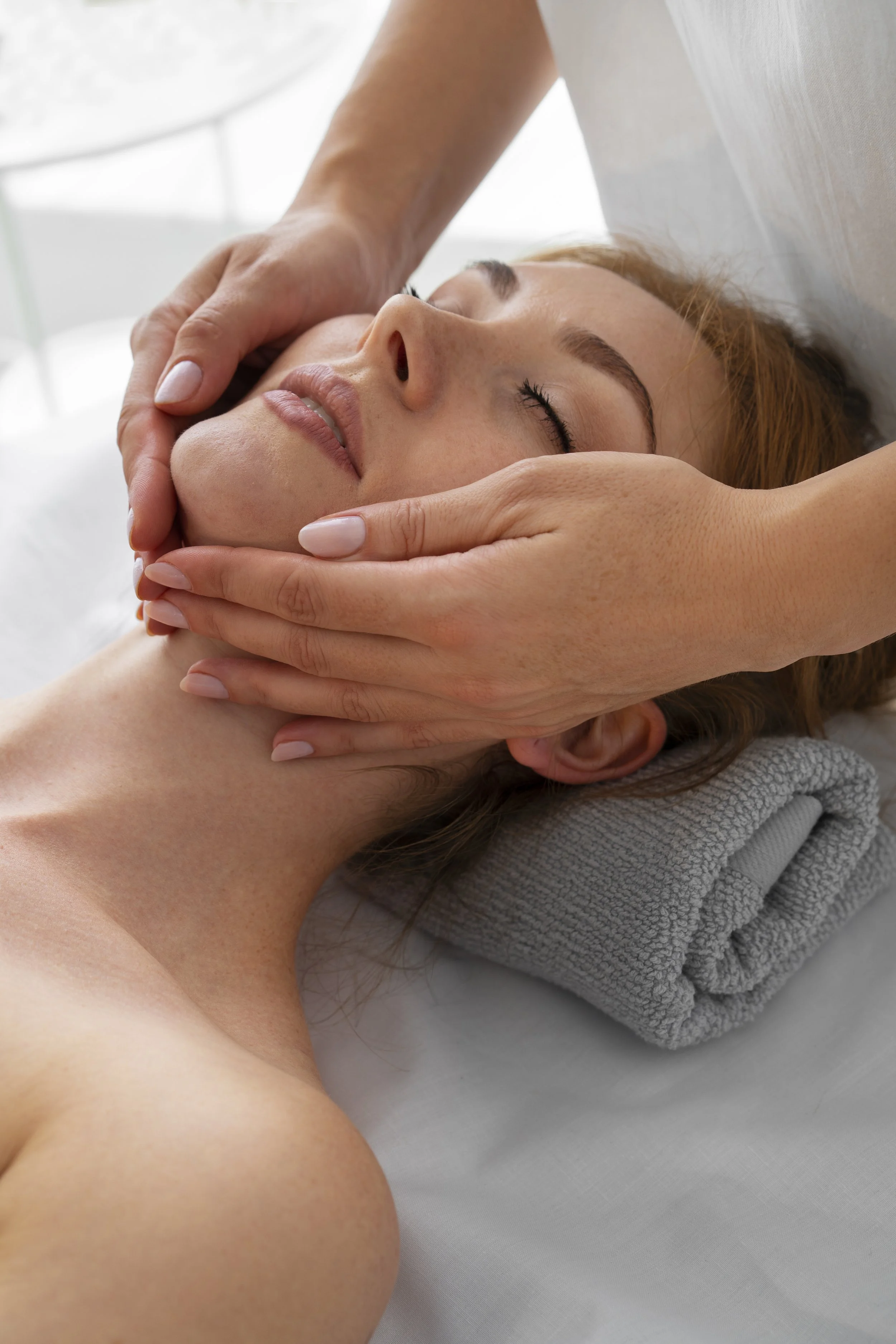 A woman receiving a facial massage from a massage therapist in a spa or wellness center.
