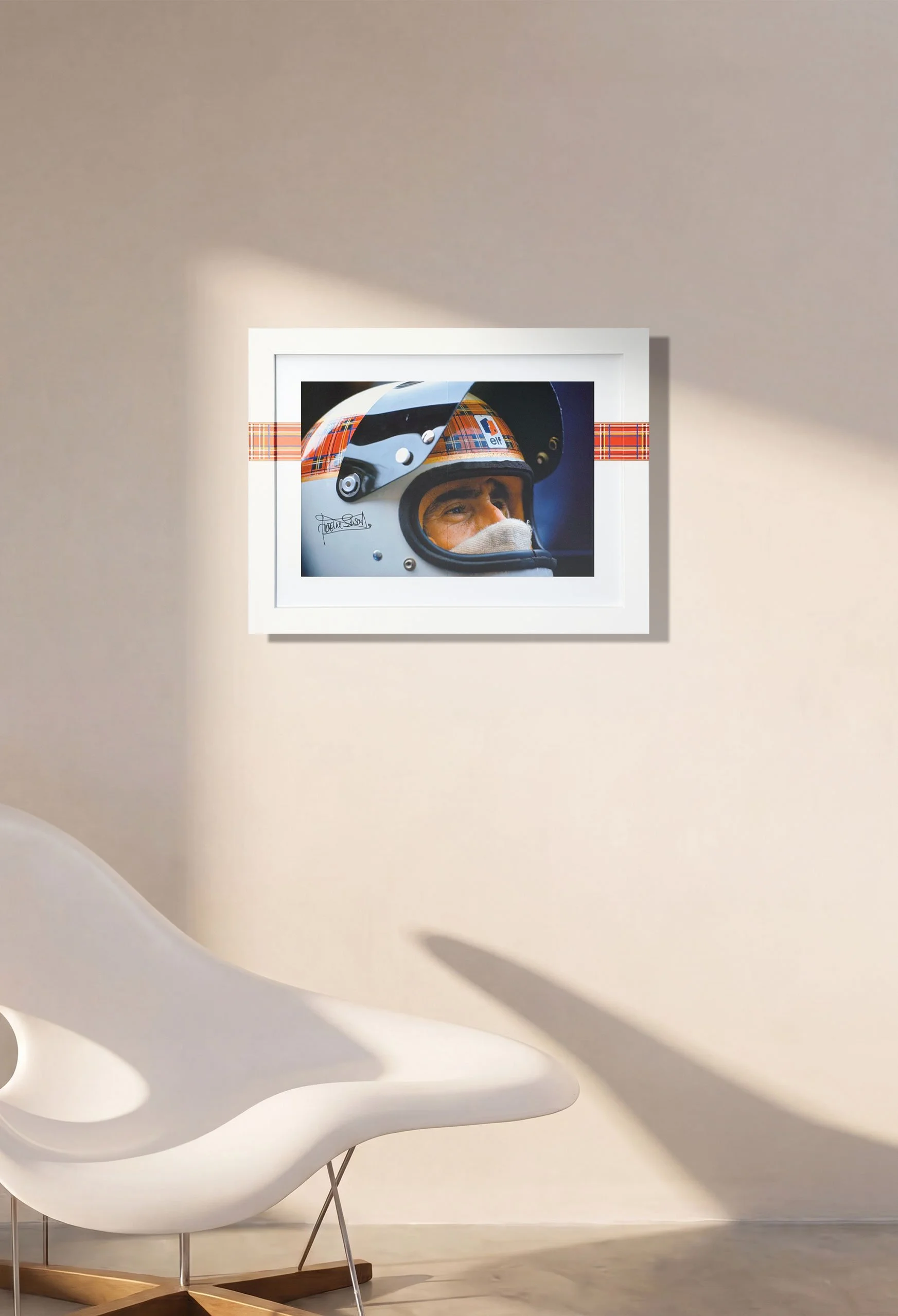 Framed photograph of a race car driver wearing a helmet with plaid and EMO branding, on a white wall in an art gallery.
