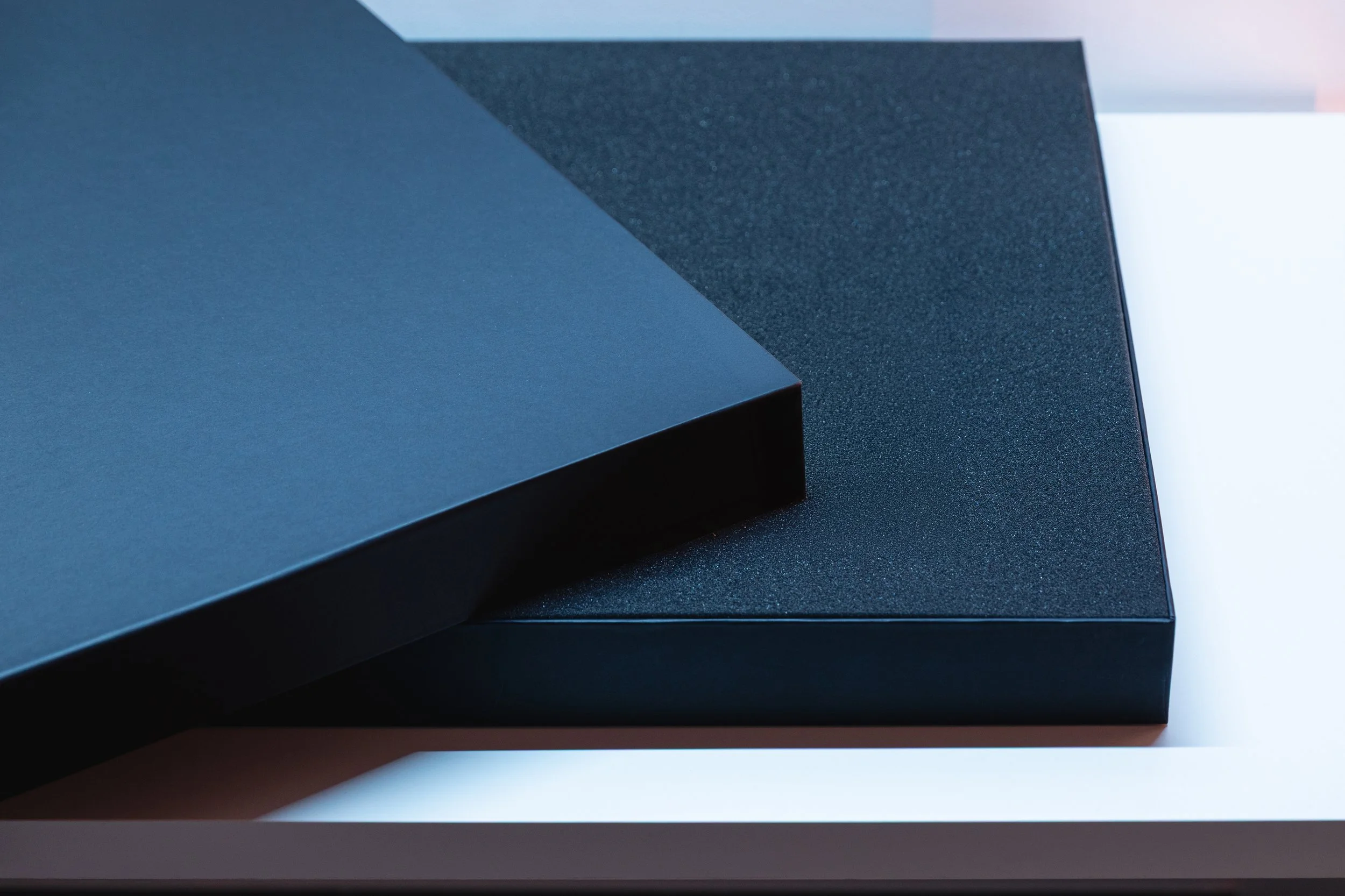 Close-up photo of stacked dark-colored books with textured covers on a white surface.