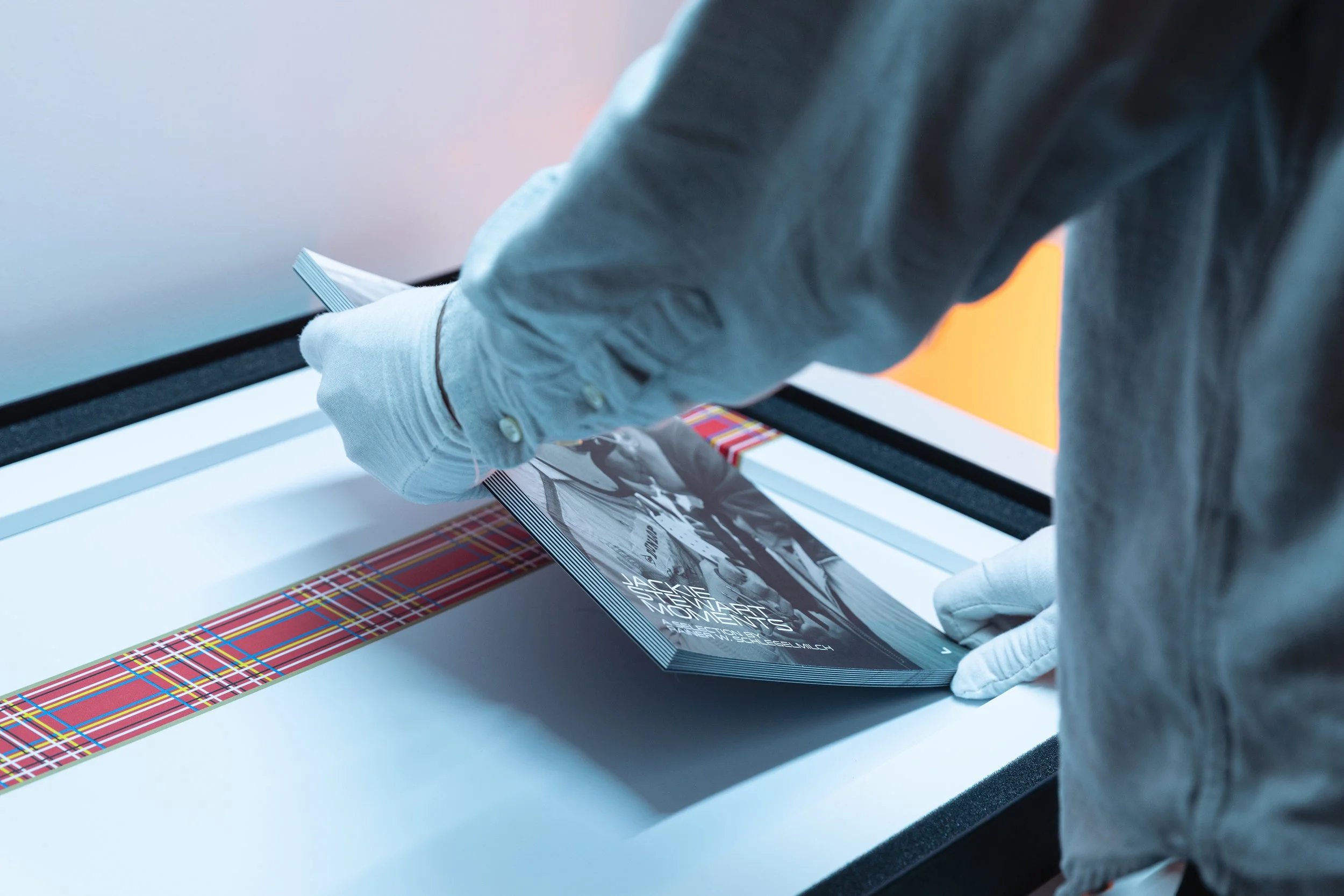 Close-up of a person wearing a gray shirt and white gloves, handling a vinyl record album covering on a white table.