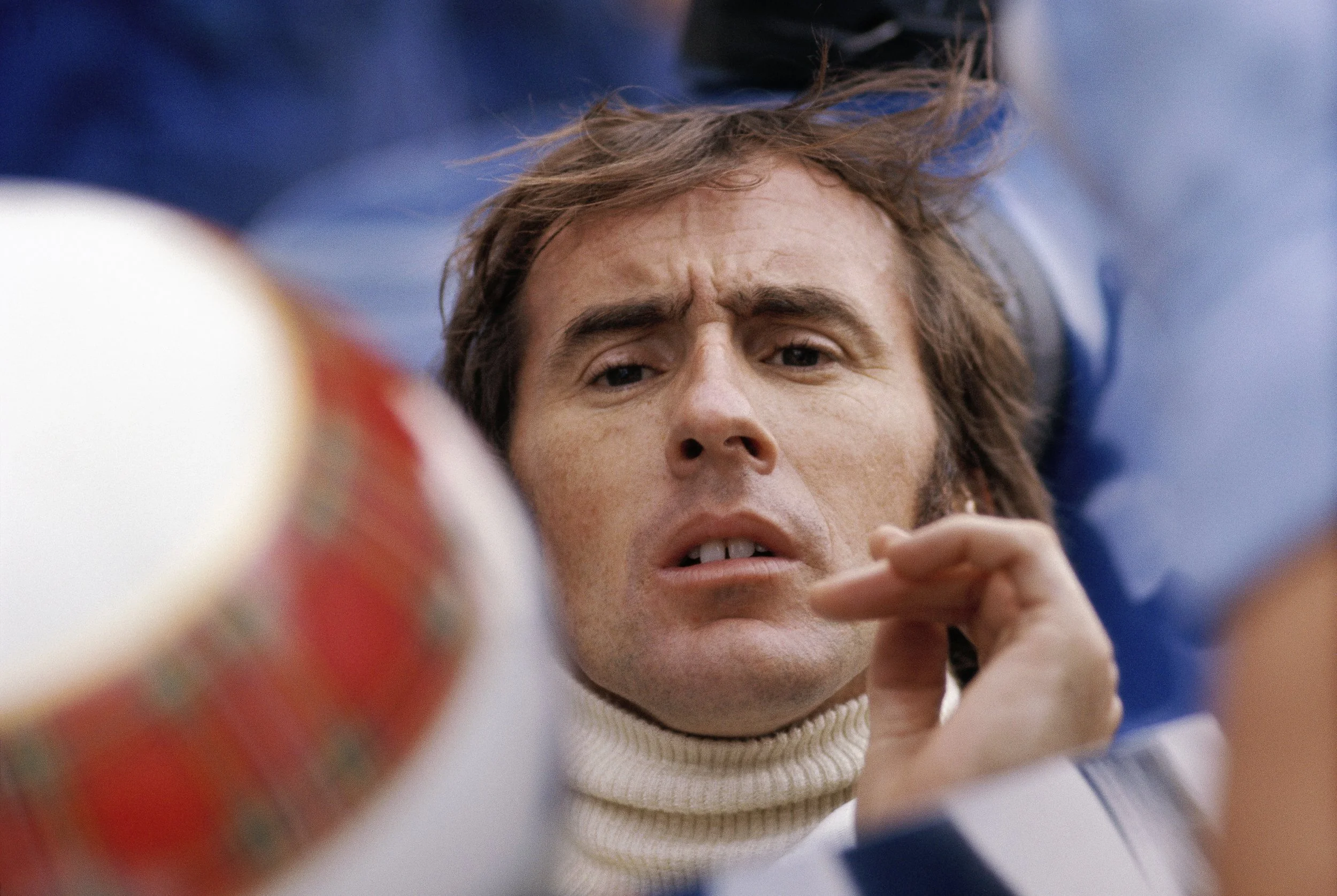 Close-up of a person's face with curly brown hair, wearing a cream-colored turtleneck sweater, looking intently at something, with a blurred background.