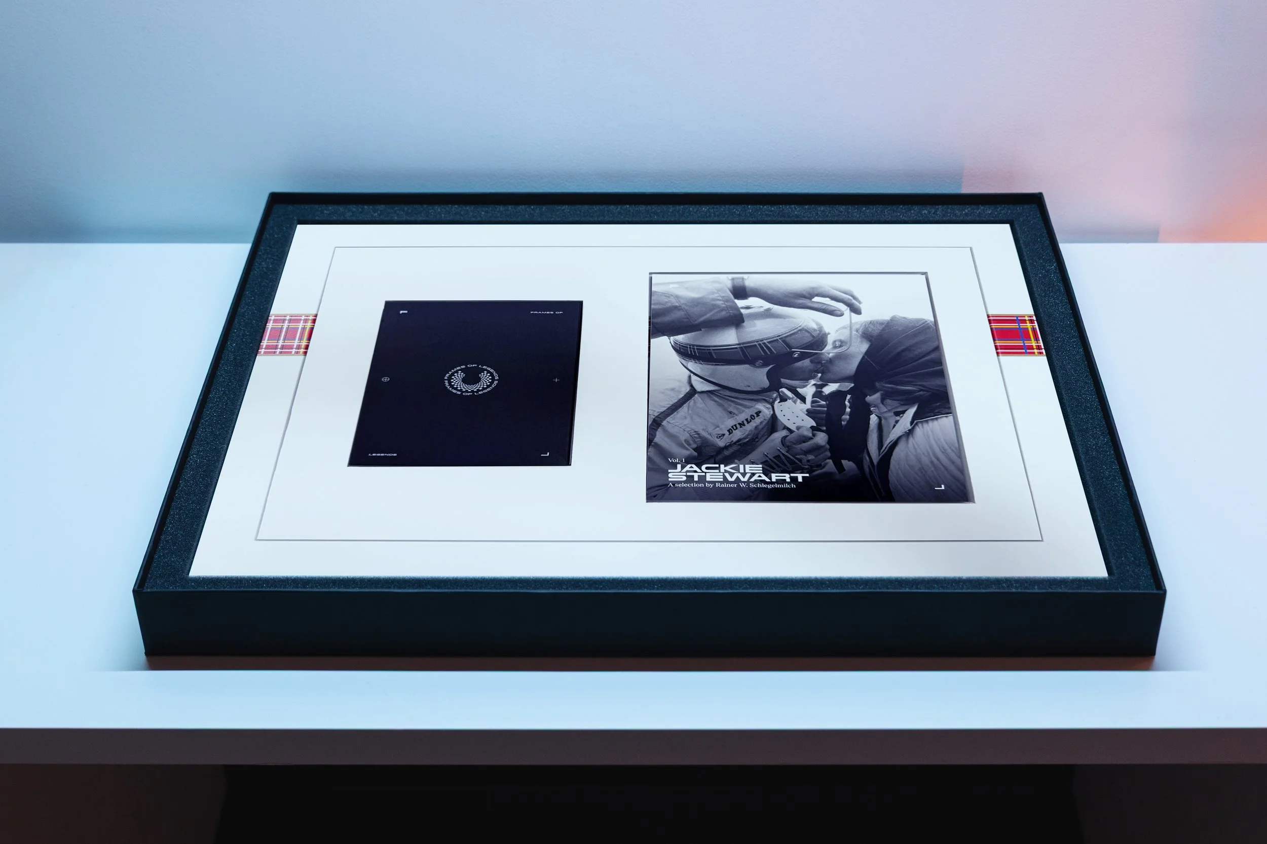 A framed black and white photograph of a hand adjusting a guitar, accompanied by a black rectangular booklet or card, all displayed on a white surface with a dark border.