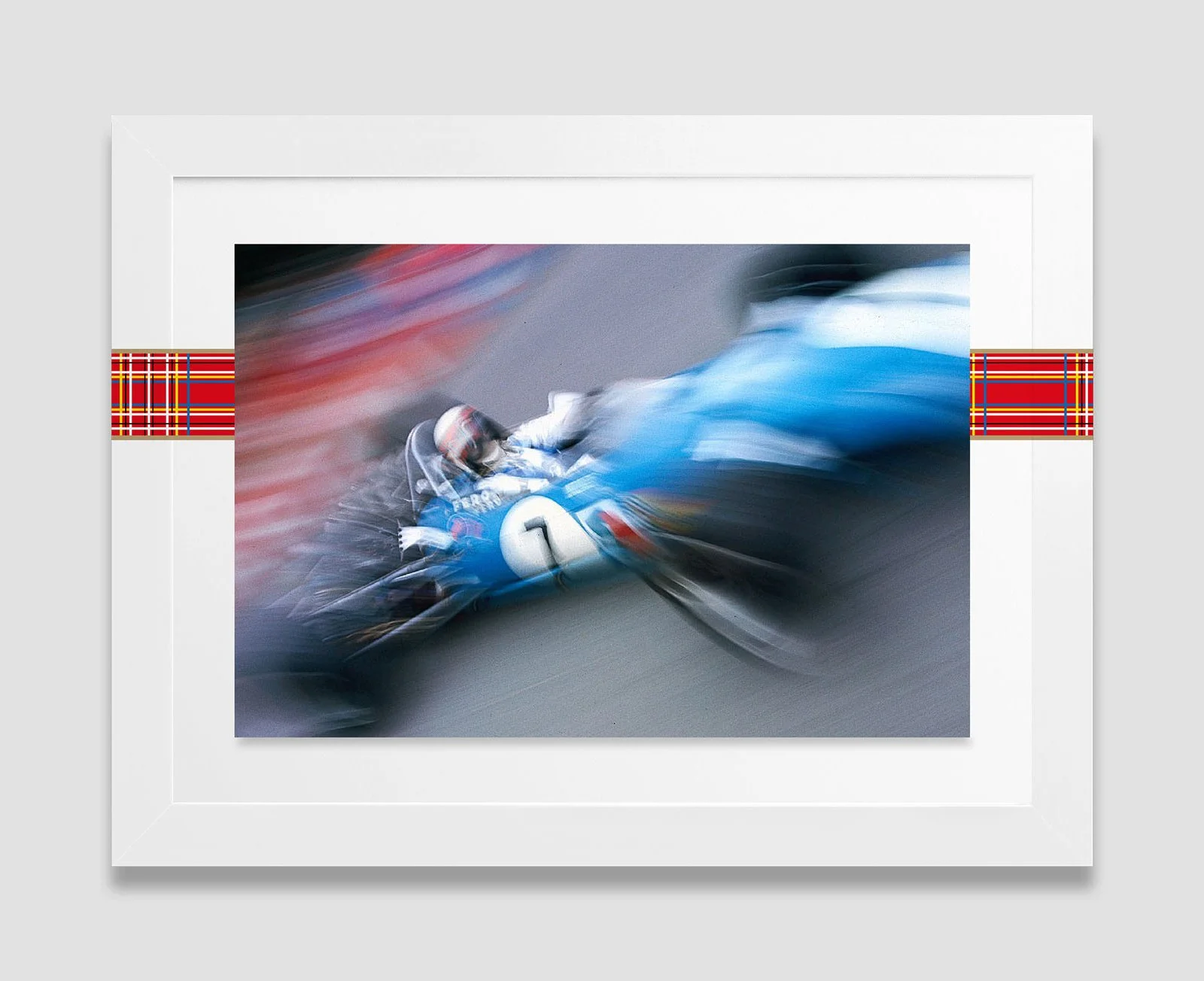 A framed photograph of a racing car in motion, with a driver wearing a helmet, on a racetrack. The image features a motion blur effect, emphasizing the speed of the car.