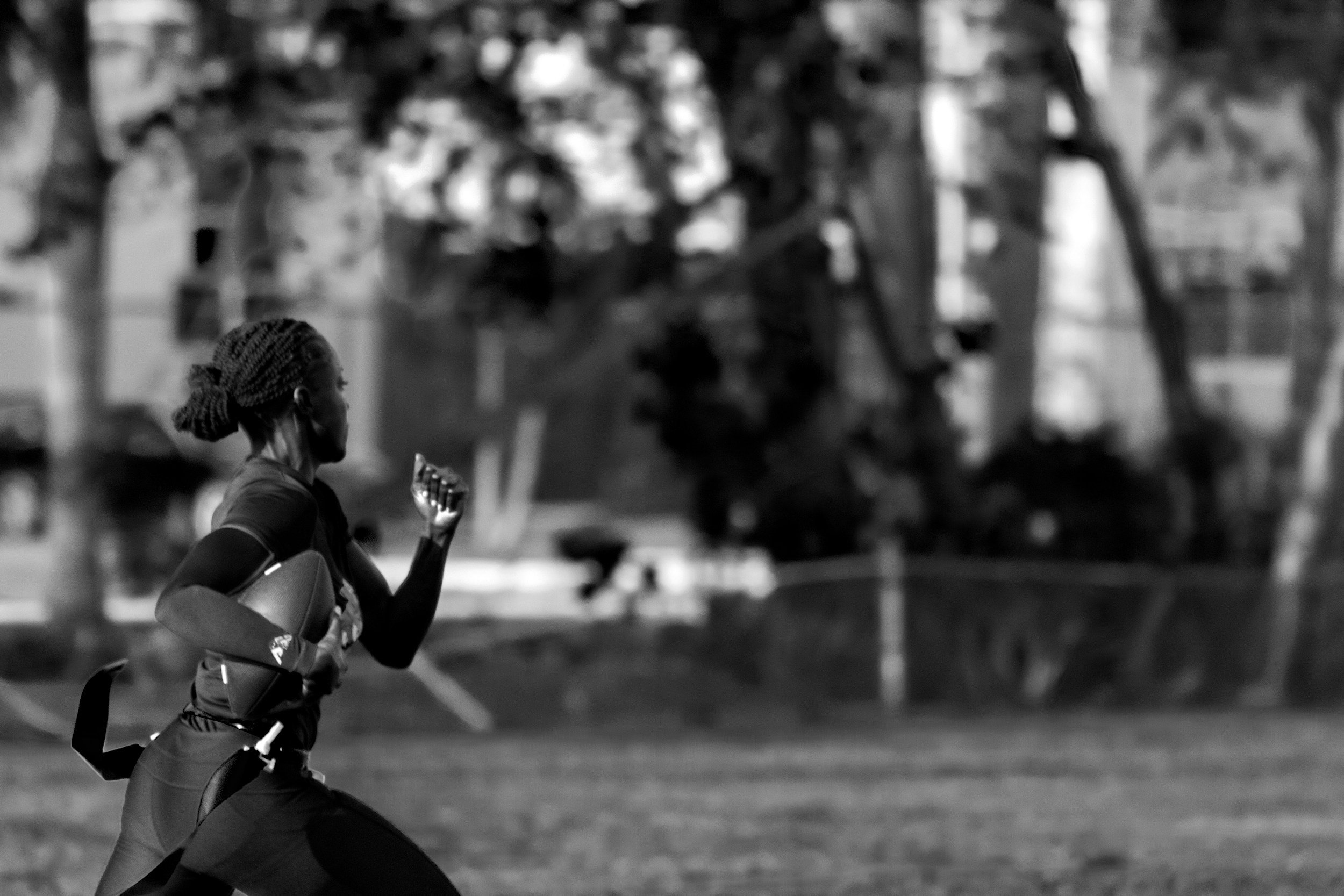 A woman running outdoors on a grassy field, carrying a football, with trees in the background.