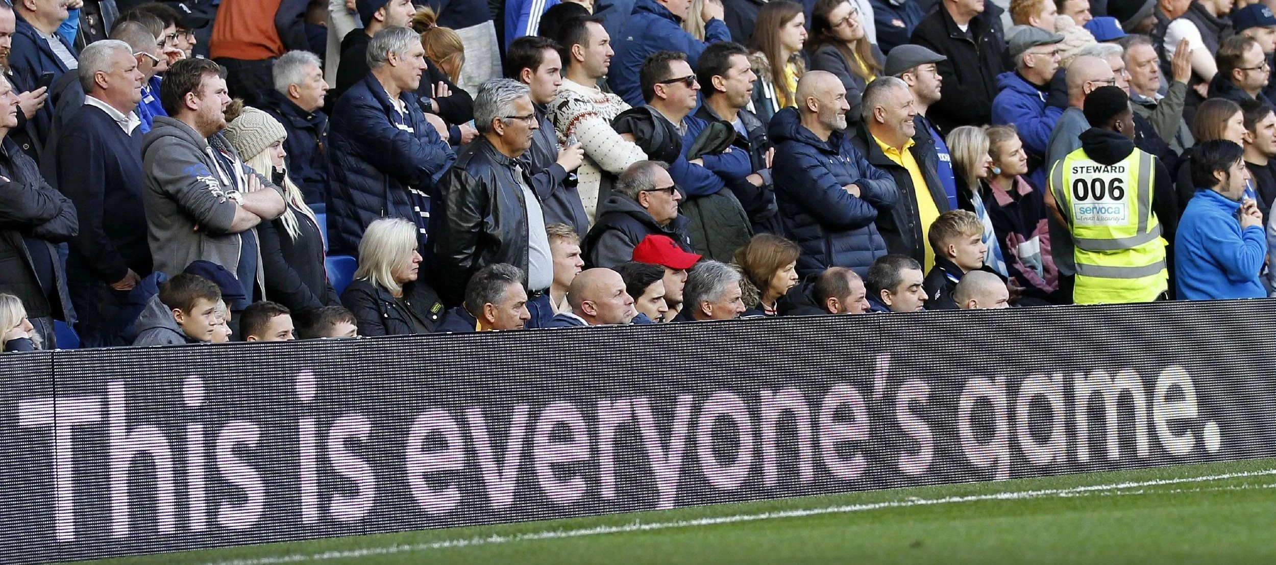 Football fans in the stands with “This is Everyone’s Game” message displayed on stadium boards.