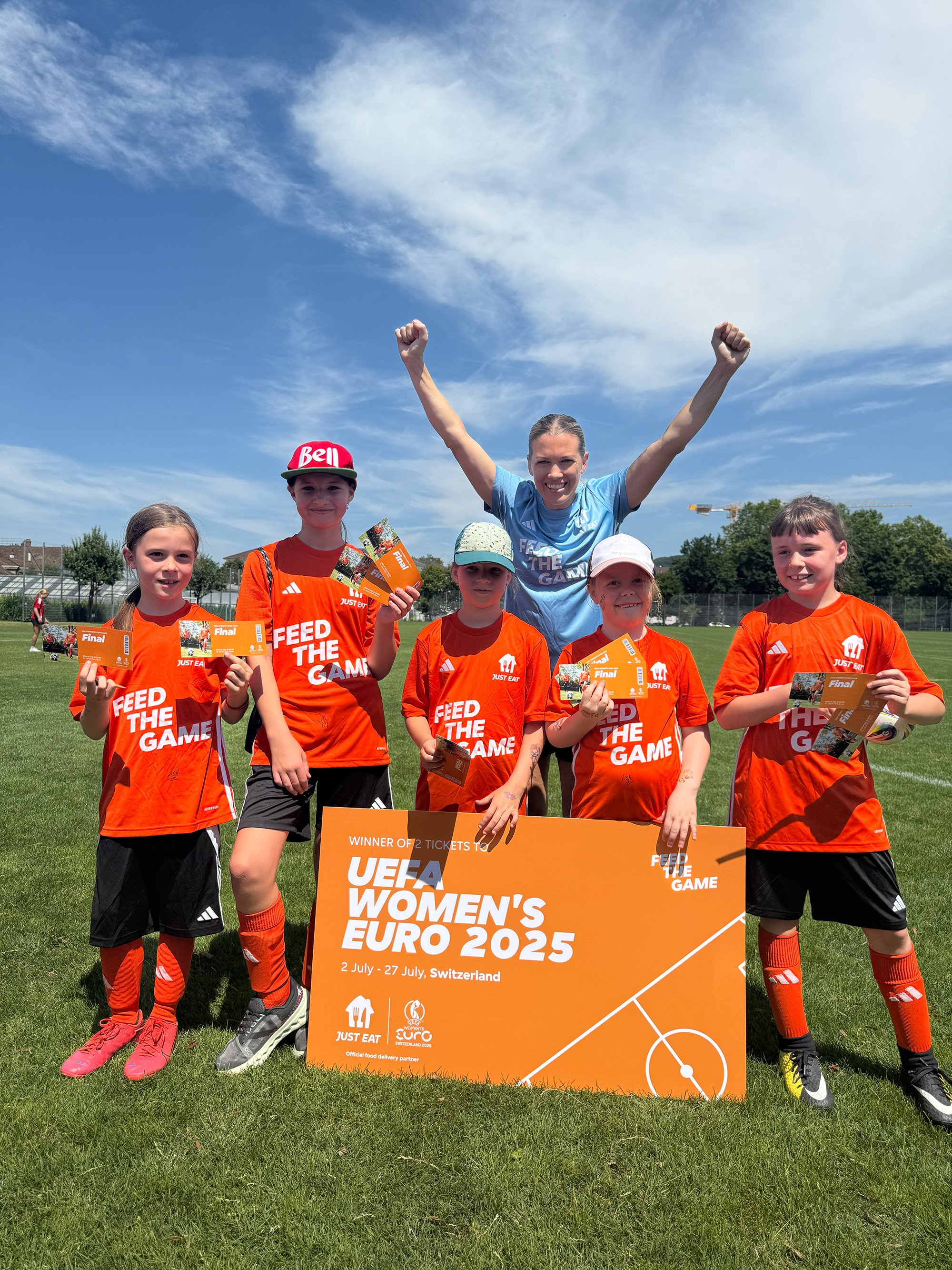 Lara Dickenmann raises her arms as girls hold a “Feed the Game” sign.