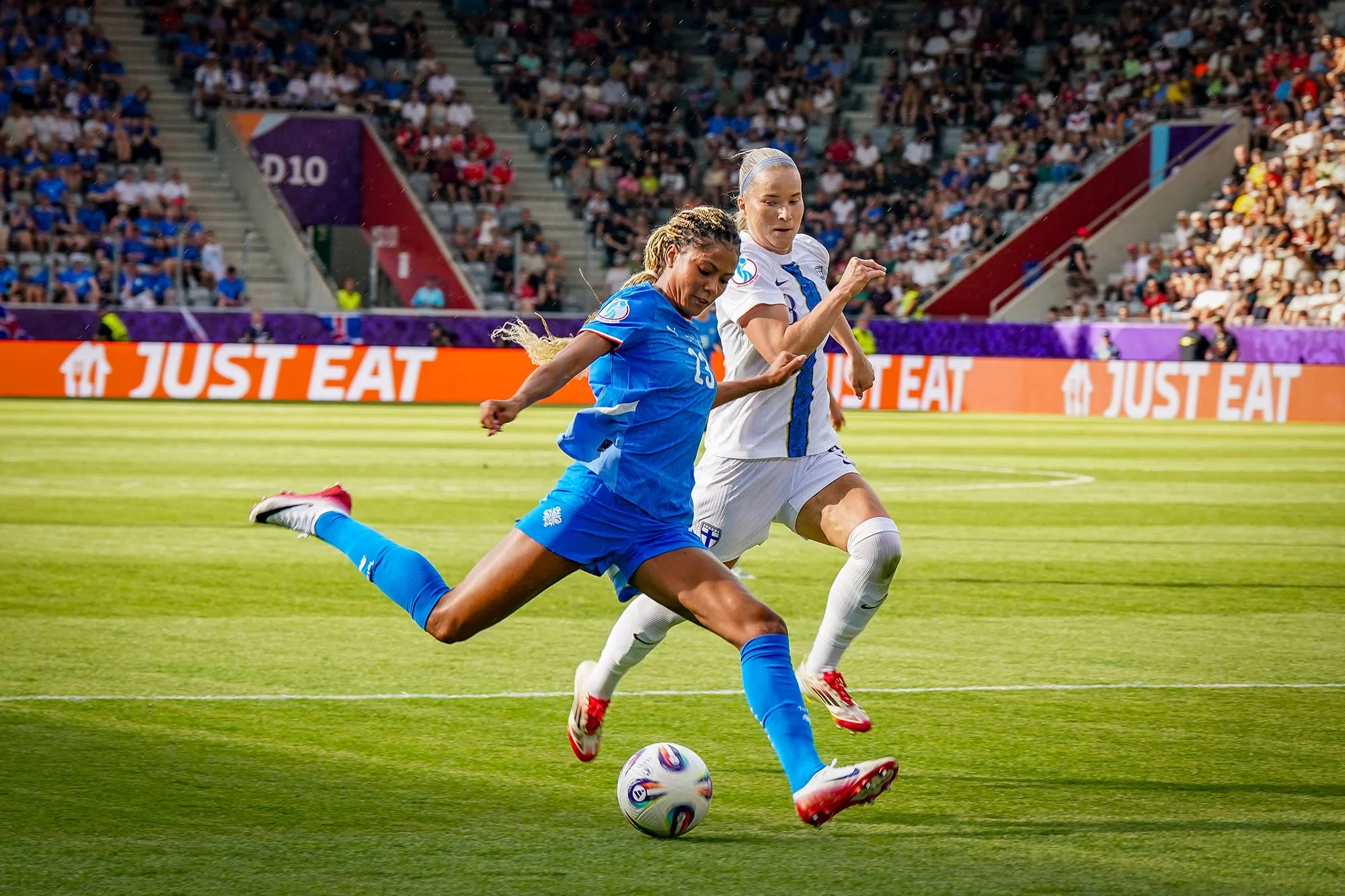 Two women football players in action during a UEFA Women's Euro 2025 match in Switzerland, with Just Eat branding visible on stadium advertising boards