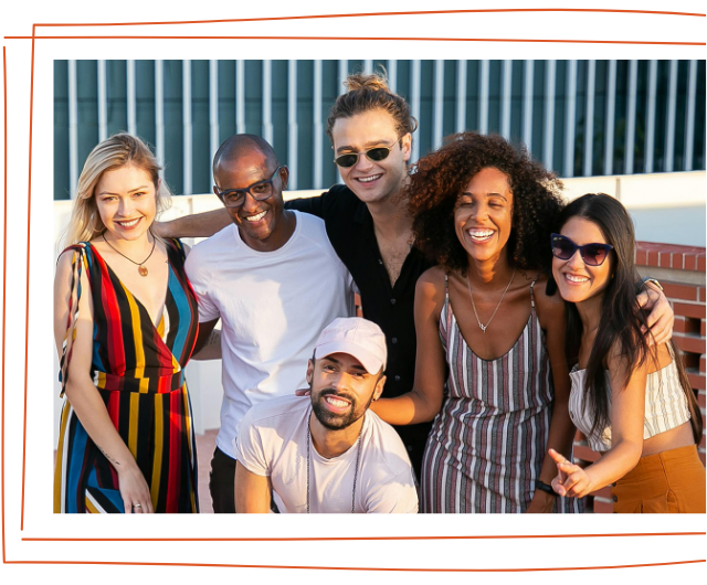 Group of six friends smiling and posing together outdoors on a balcony or rooftop, with a cityscape in the background.