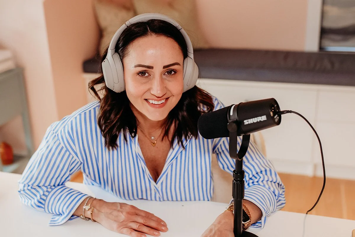 A woman wearing headphones and a striped shirt, smiling into a microphone.