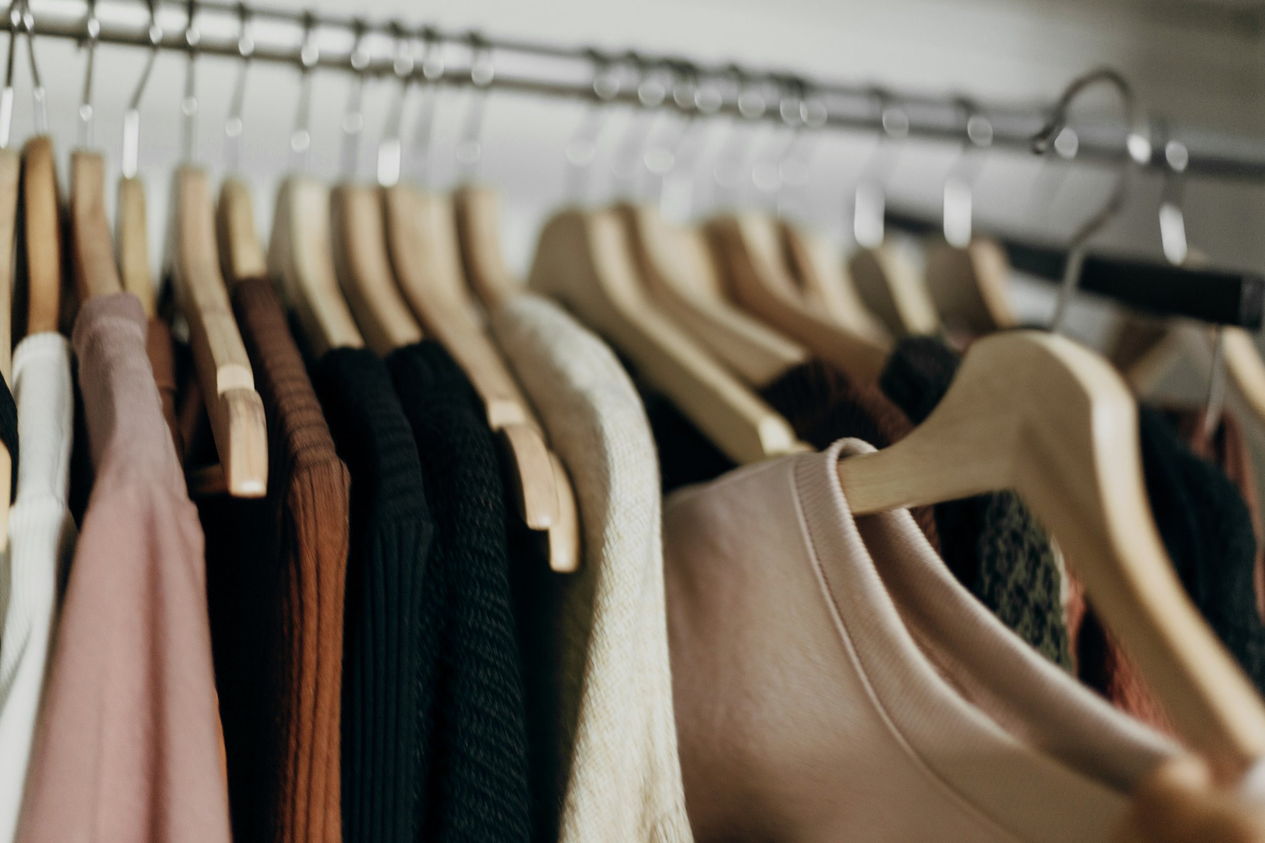 Blick in einen Kleiderschrank mit verschiedenen T-Shirts und Pullovern in verschiedenen Farben auf Kleiderbügeln an einer Garderobenstange.