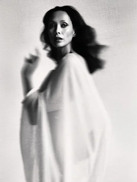 A black-and-white portrait of a woman with dark wavy hair, wearing a loose, light-colored garment, looking directly at the camera with a serious expression. Ai Generated, Creative direction with  AI 