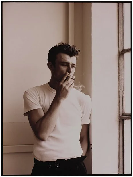 A man in a white t-shirt smoking a cigarette near a window. Ai Generated, Creative direction with  AI 