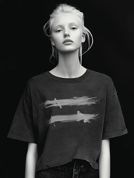 Black and white photo of a young woman with light hair, wearing a loose black T-shirt with abstract paint streaks, standing against a dark background. Ai Generated, Creative direction with  AI 