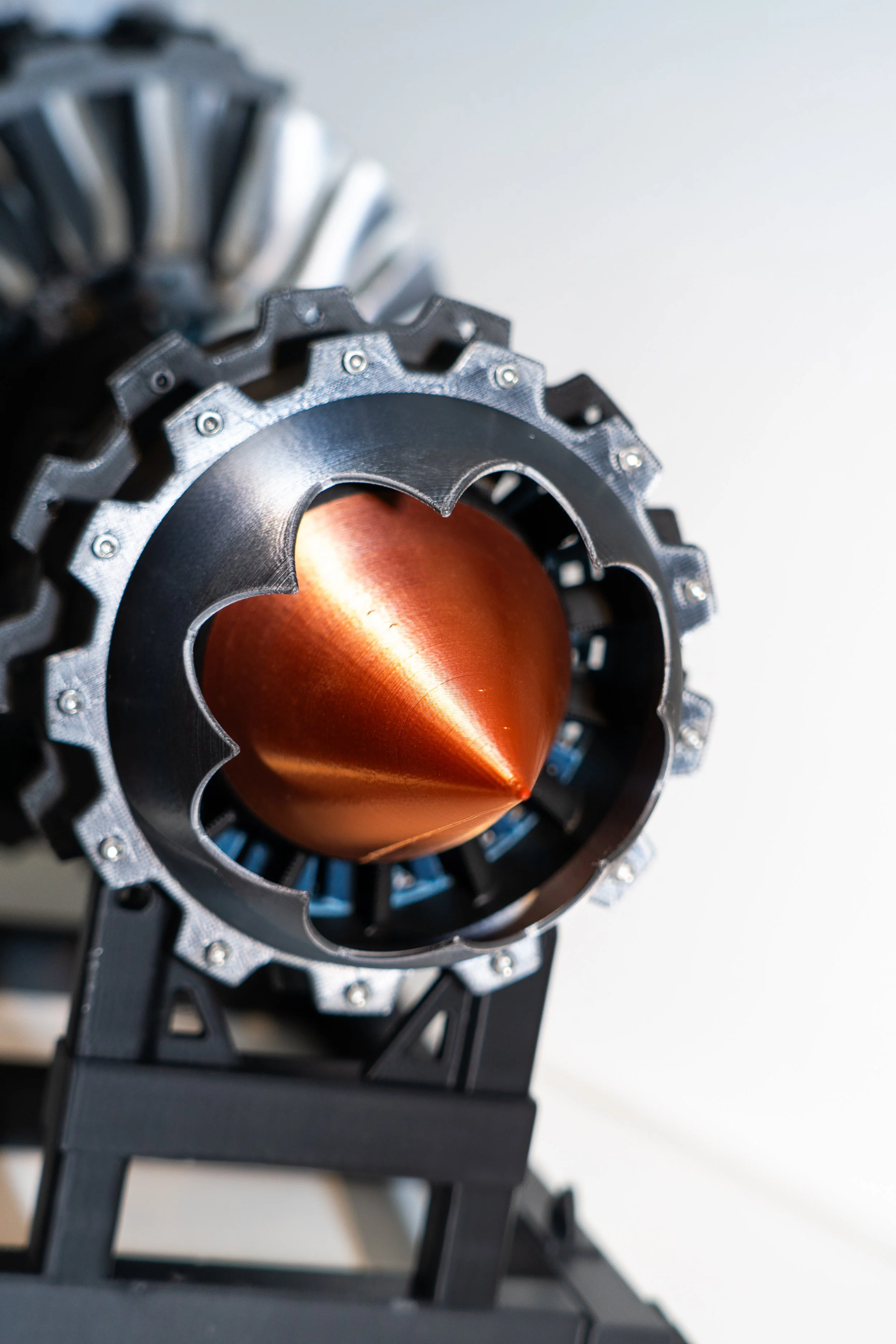 Close-up of a scientific instrument with a metallic, conical inner part and a gear-like outer structure, mounted on a black stand.