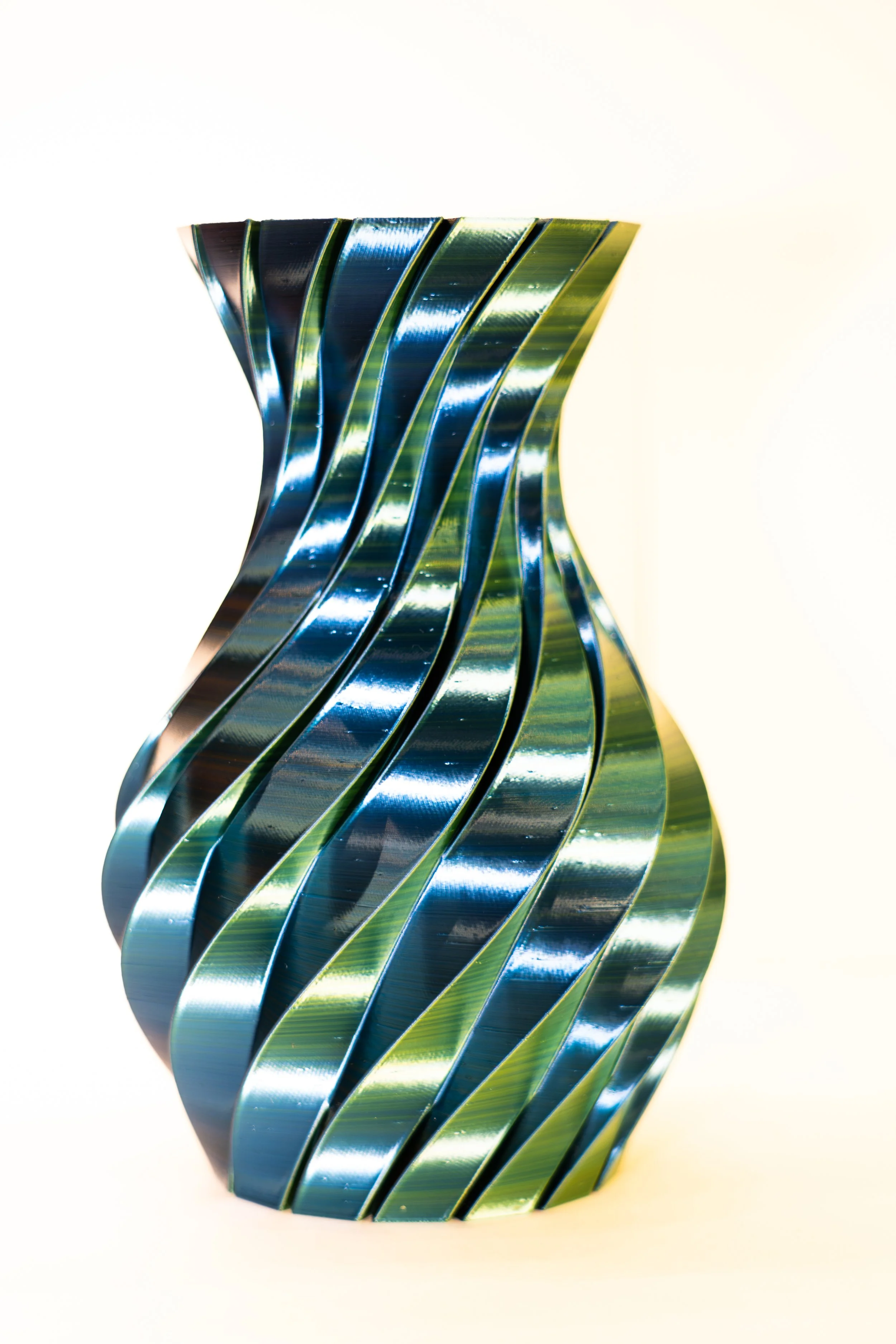 Modern metallic vase with a twisted, striped design, set against a white background.