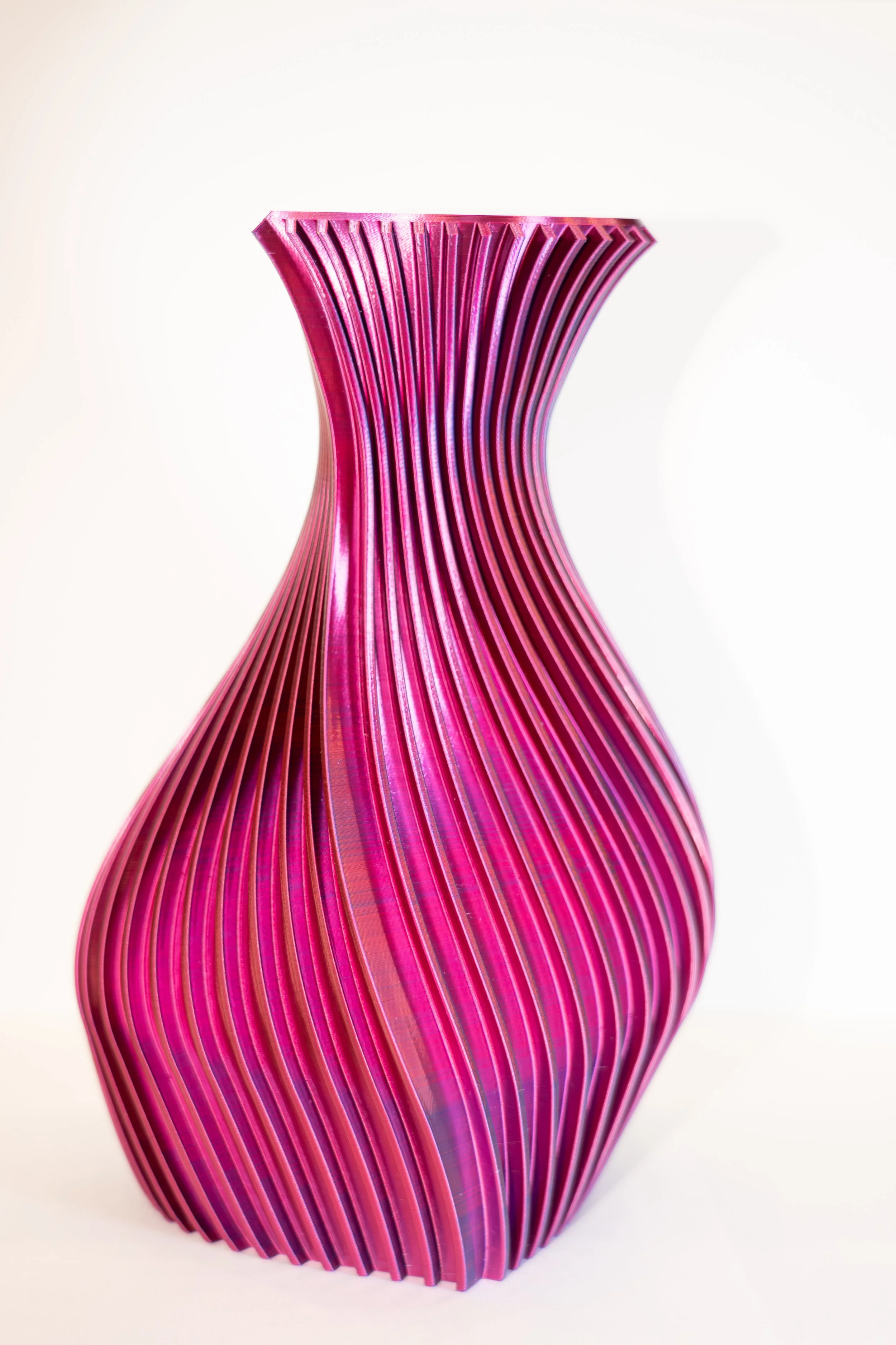 Pink, curved, ribbed ceramic vase with a glossy finish.