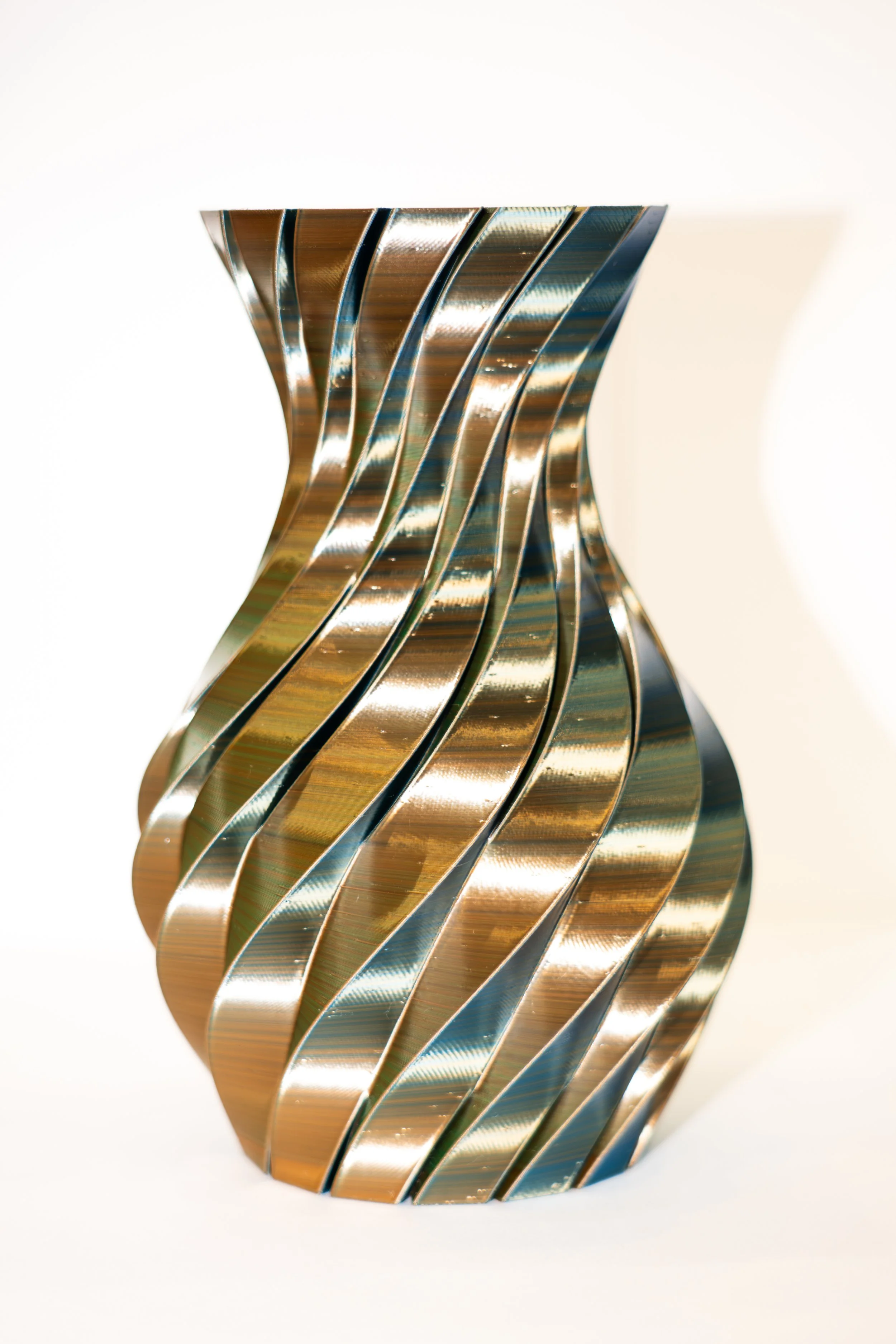 Modern metallic sculptural vase with twisted wavy vertical ridges on a white background.