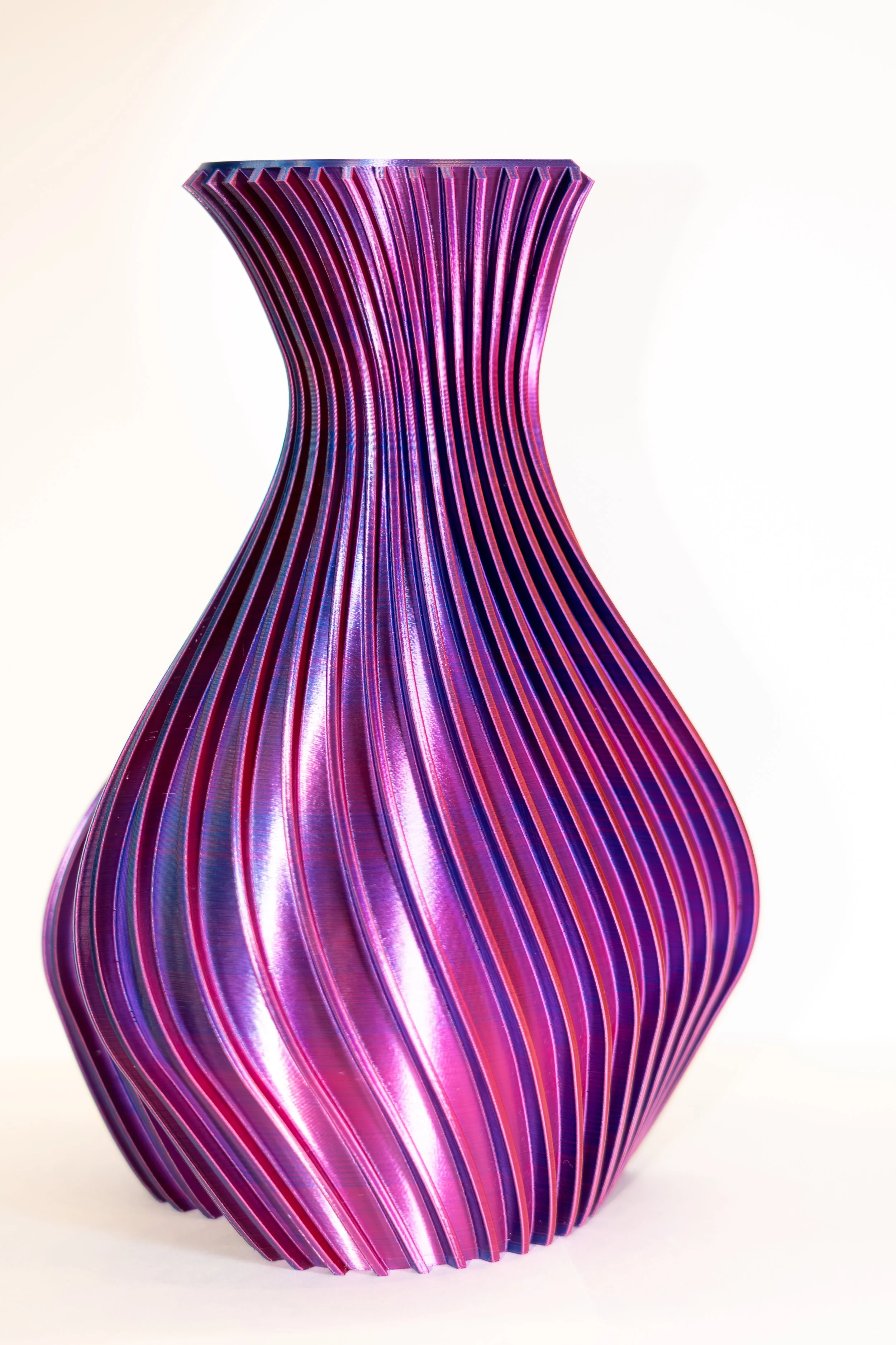 A modern, artistic vase with a metallic purple and pink striped surface featuring a twisted, wave-like design.