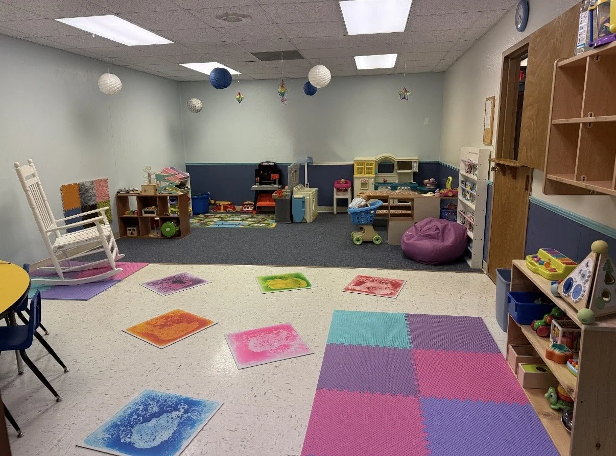 Children's playroom with colorful mats, a rocking chair, toys, and play kitchen set, decorated with hanging paper lanterns and star ornaments.