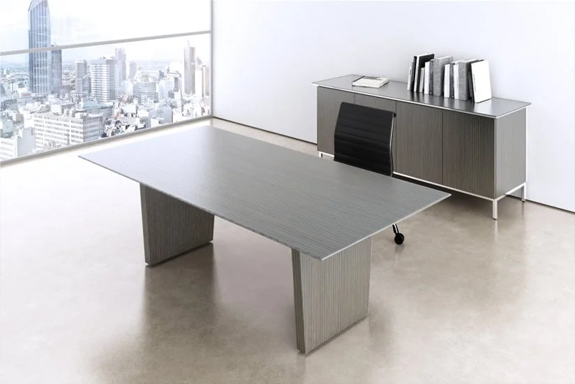 Modern office with a large desk, black office chair, and a cabinet with books against a white wall, overlooking a city skyline through large windows.
