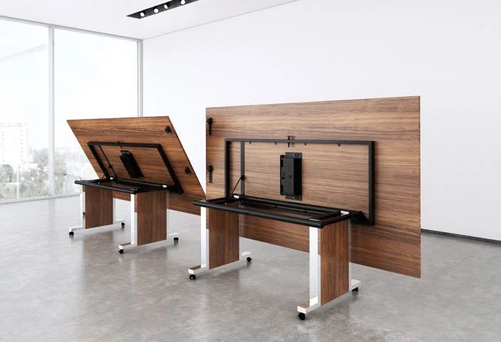 Two large wooden tables with adjustable tops and black frames, mounted on white legs, in a bright modern room with large windows and minimal decor.