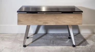 Mid-century modern wooden coffee table with black top and angled metal legs in a room with hardwood floor.