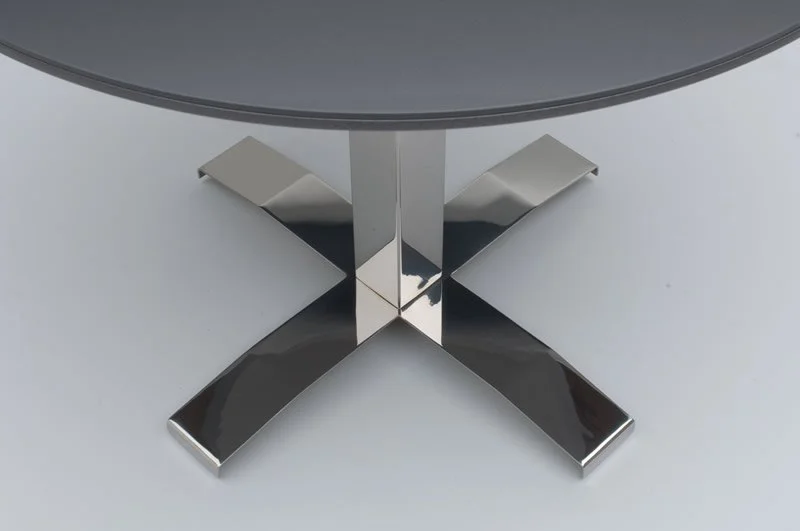 Close-up of a Nextt Cross Base round community table with dark natural stone tabletop and chrome base.