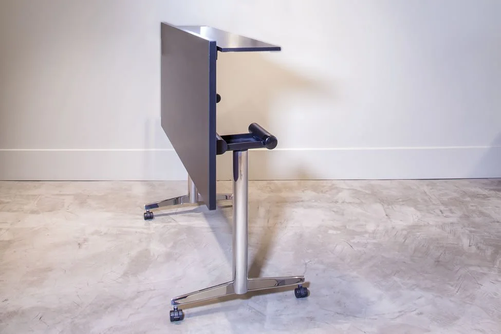 Asteri training table flipped up for storage with dark wood veneer tabletop and a chrome base.
