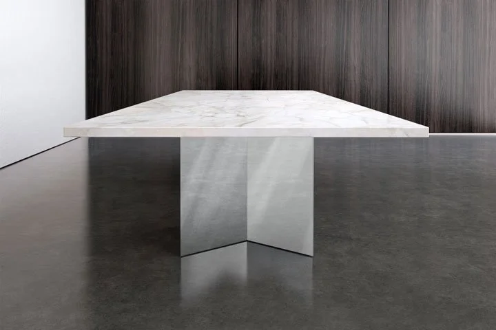 Modern minimalist table with a white marble top and concrete base, set against dark wood wall and gray flooring.