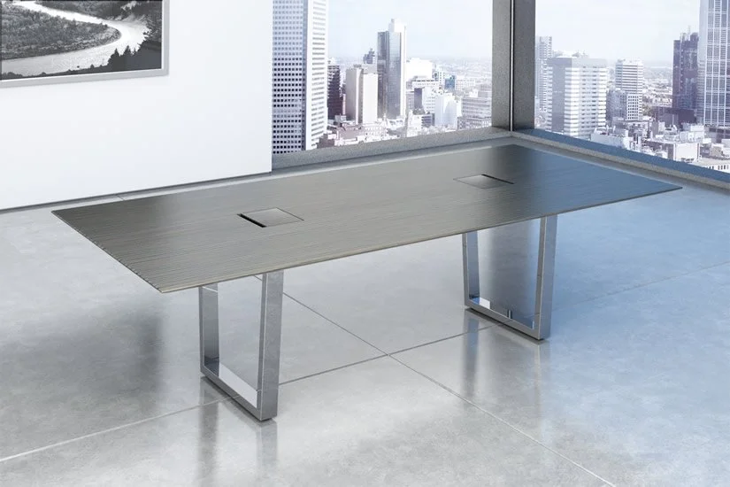Modern office conference table with built-in power outlets, situated in a high-rise office with city skyline view through large windows.