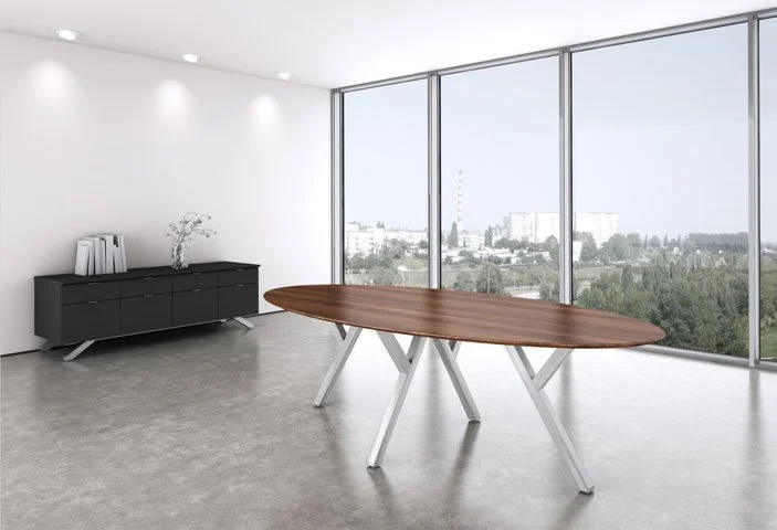 Oval 2Merge table with wood tabletop and brushed aluminum base. Credenza in the background of a modern office with large windows looking outside.