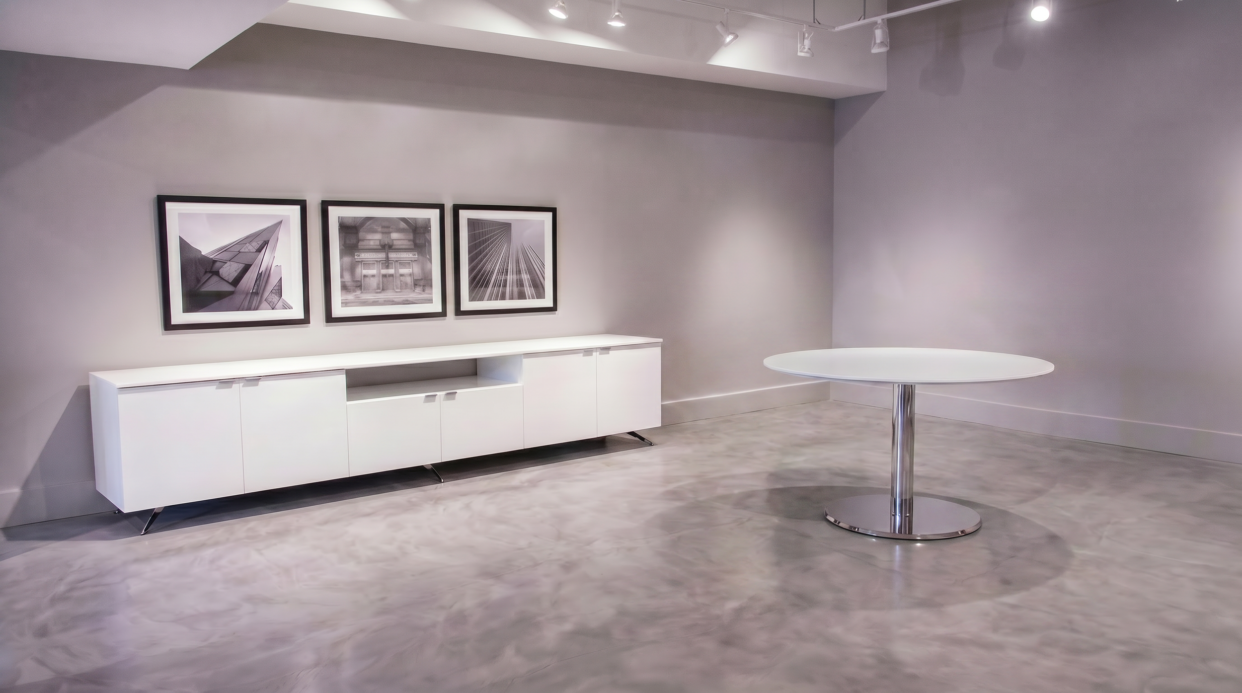 A large room with a white credenza and a round Beveled Plate table with a white painted back grass tabletop and a chrome base.
