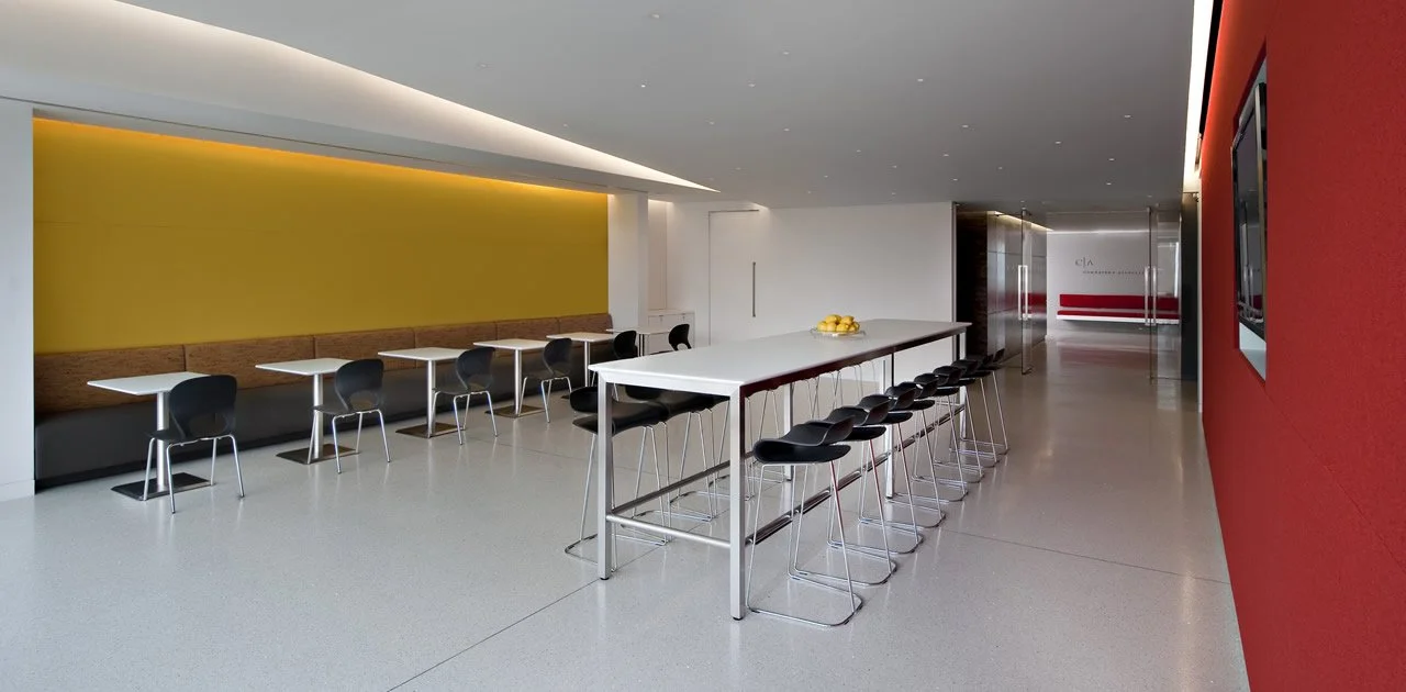 Modern high community table with stool and cafe tables for two along the wall.