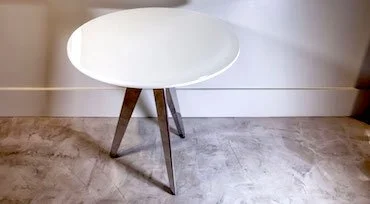 Round white table with wooden tripod legs in a room with gray carpet and beige walls.