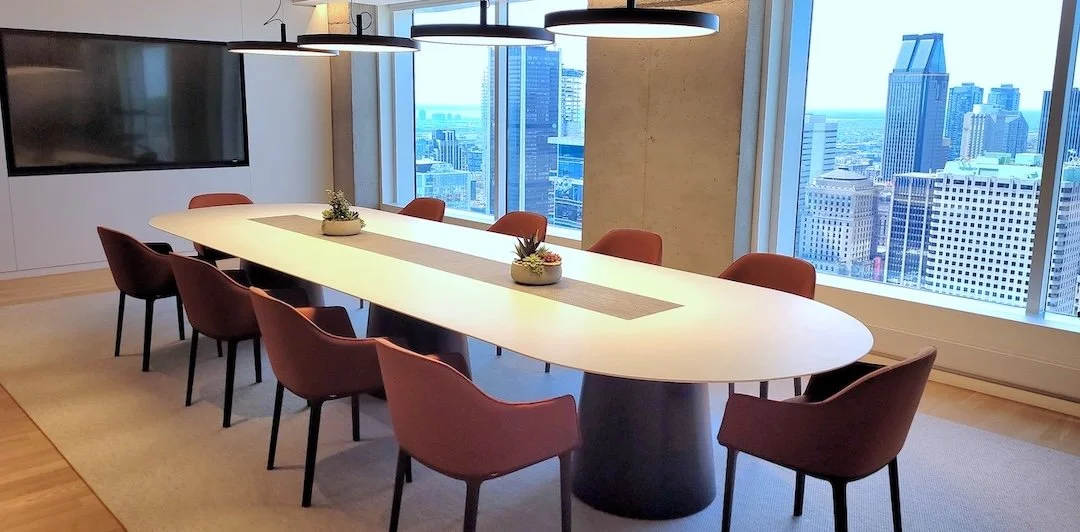 Modern conference room with a long white oval table, surrounded by nine maroon chairs, set in front of large windows with a city skyline view.