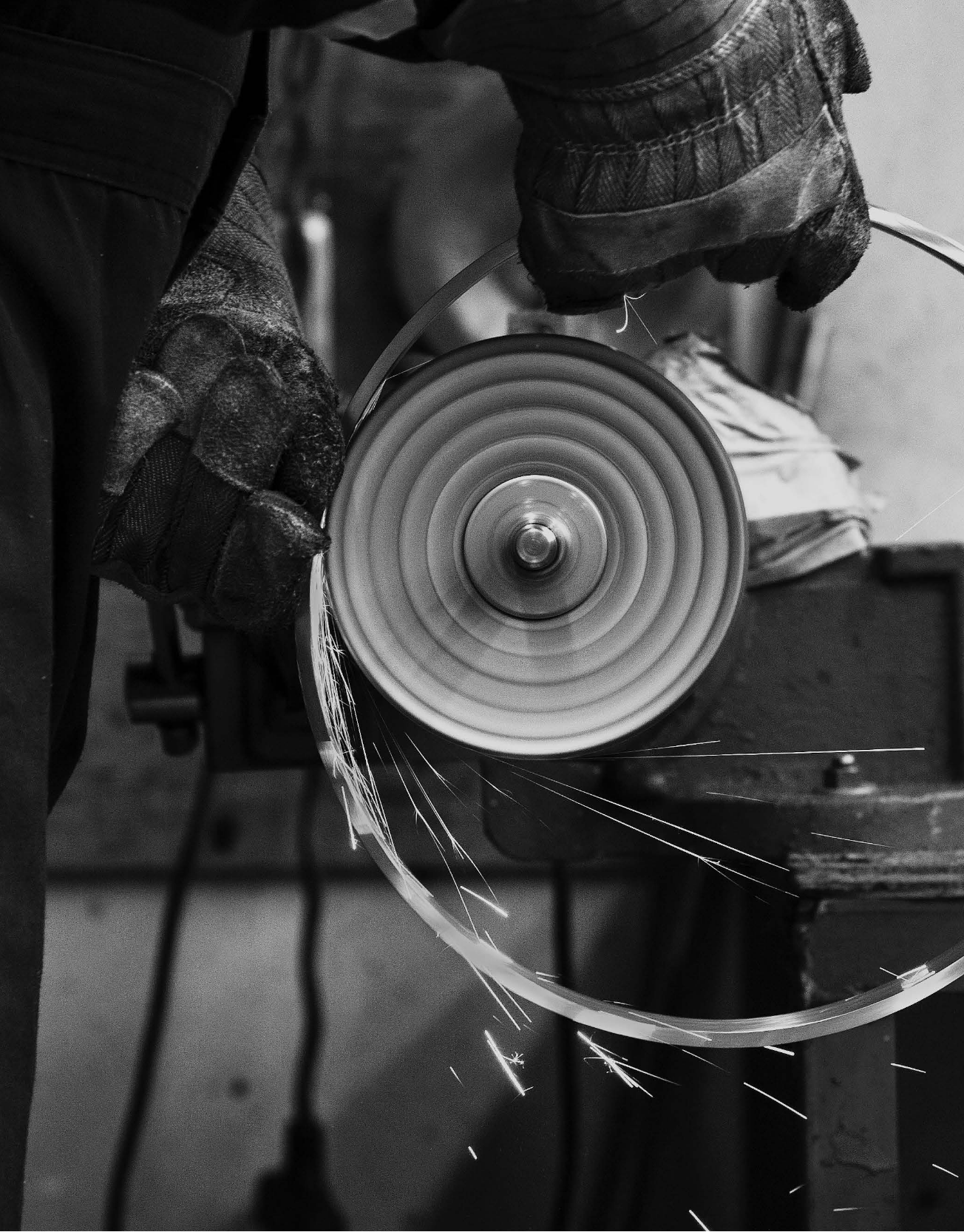 A craftsman works with a strip of metal on a grinder as sparks fly.