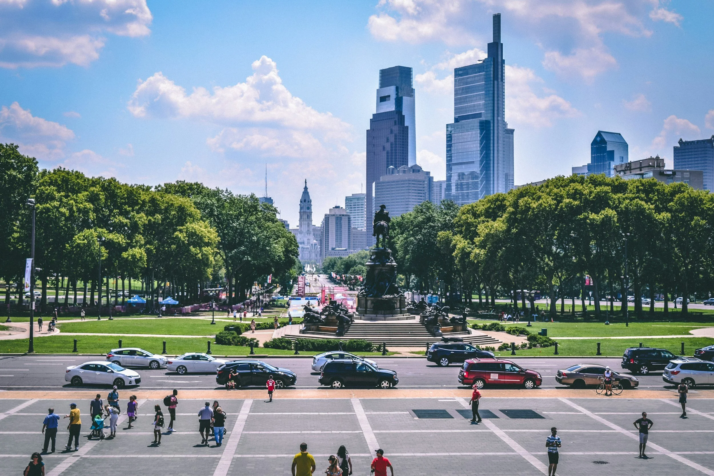 City park in Philadelphia with a monument surrounded by trees in a green space, tall modern skyscrapers, and a Clear blue sky in the background.